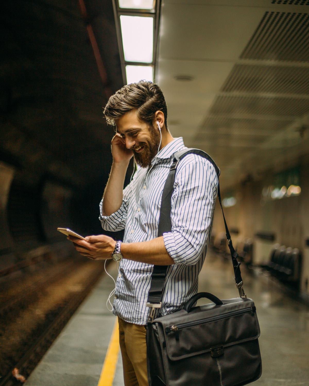 Commuter at a metro platform checking a phone, wearing headphones and carrying a work bag, representing convenient transit access near Latitude Apartments in Arlington, Virginia.
