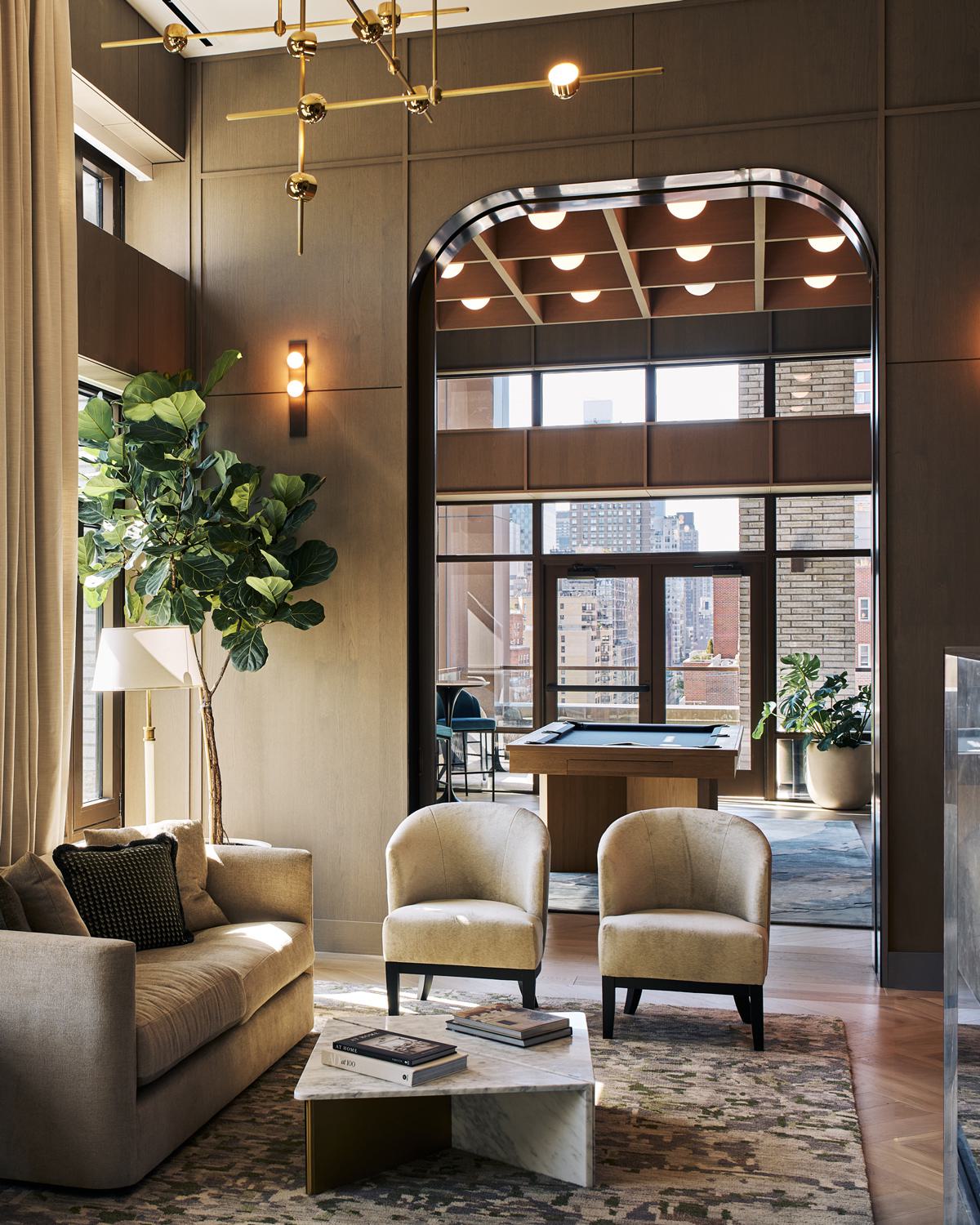 stylish game room with a wooden pool table, high ceilings, and floor-to-ceiling windows that offer a city view, complemented by warm wood paneling, elegant wall sconces, and cozy bar seating.