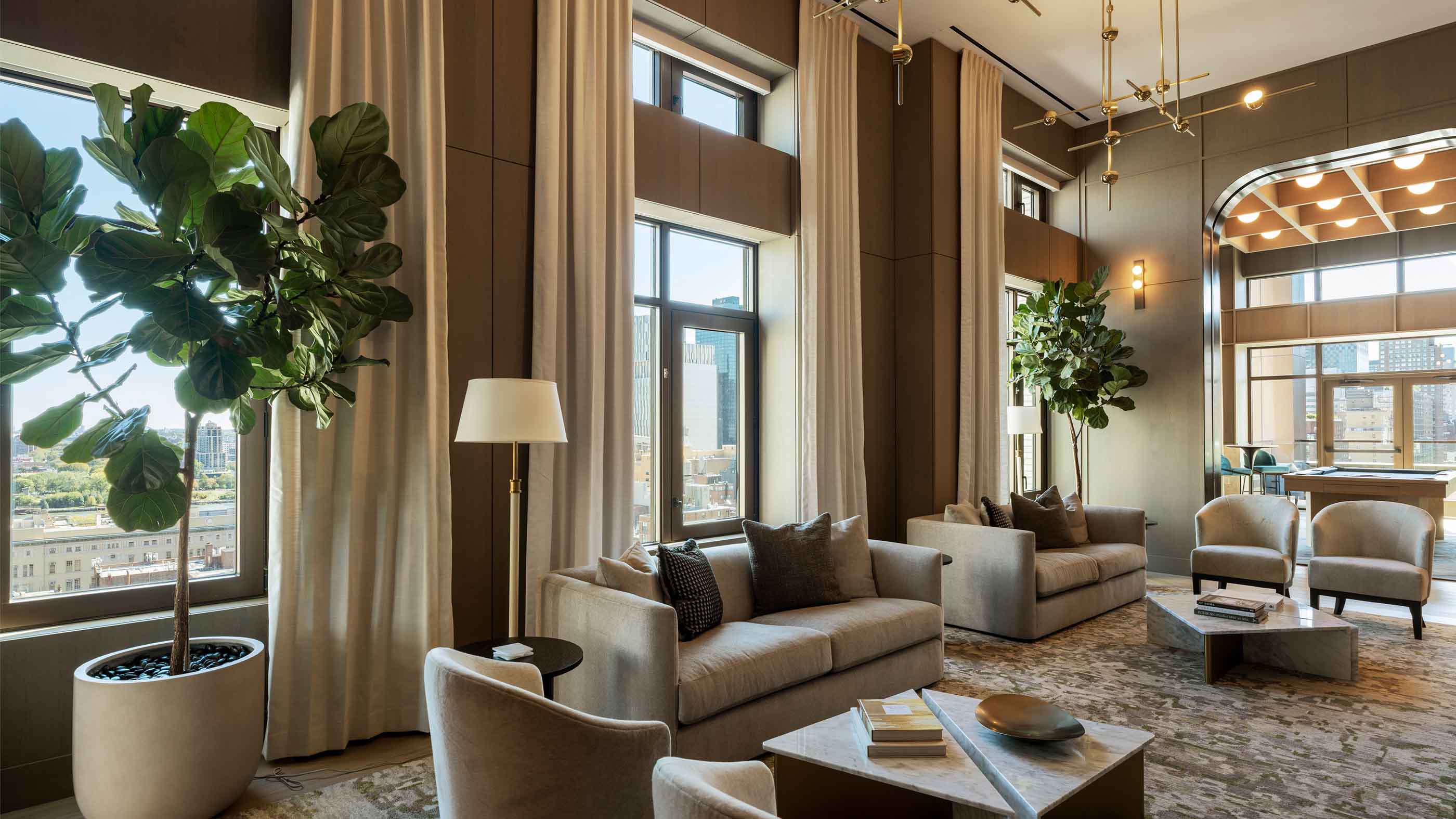 stylish game room with a wooden pool table, high ceilings, and floor-to-ceiling windows that offer a city view, complemented by warm wood paneling, elegant wall sconces, and cozy bar seating.