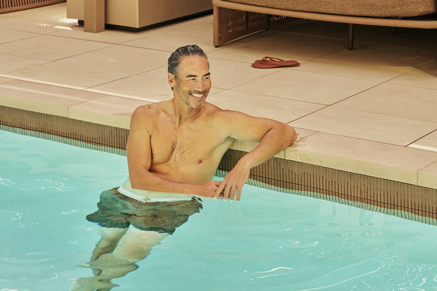 Man relaxing in the outdoor pool at Rowyn, with lounge chairs and lush planters in the background, basking in the warm San Diego sunlight.