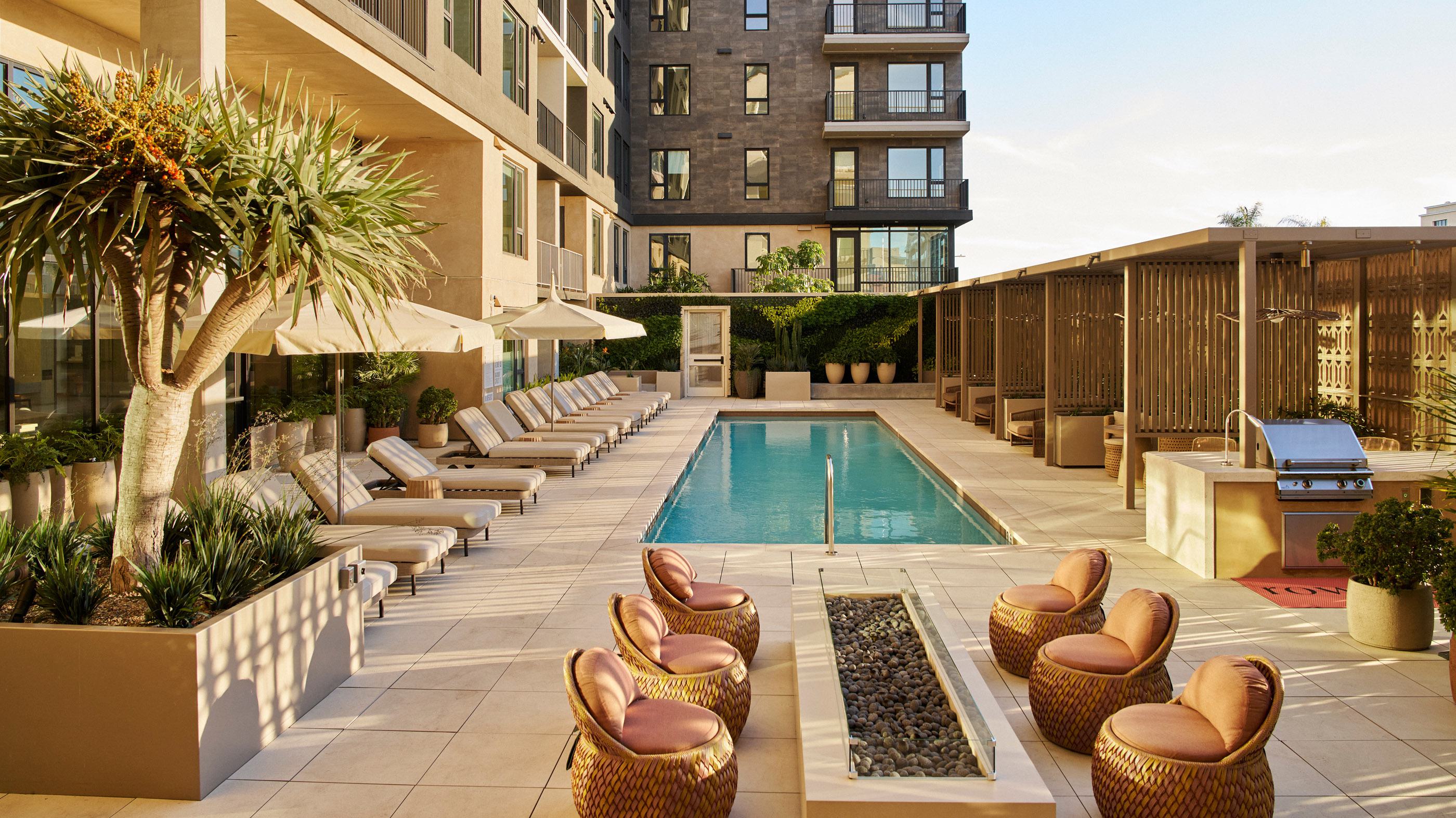 Modern outdoor pool terrace at Rowyn luxury apartment community, surrounded by cushioned lounge chairs, umbrellas, private cabanas, and lush landscaping.