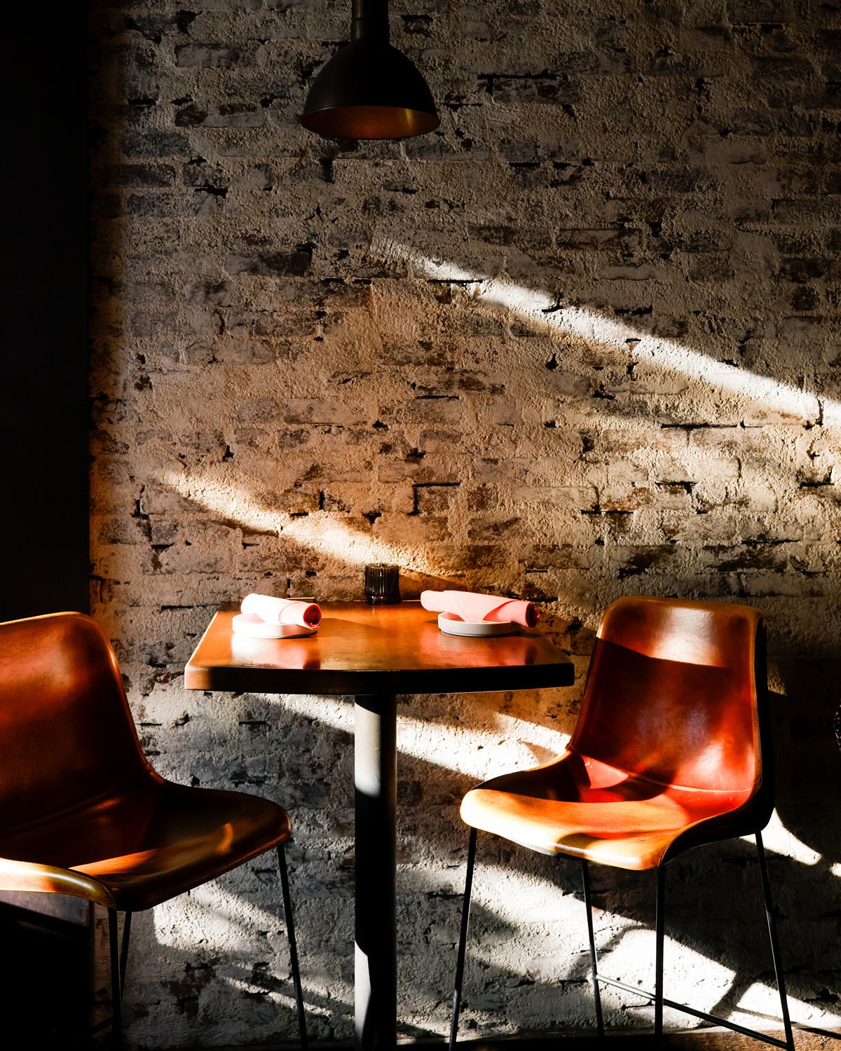 A cozy two-top dining setup in warm afternoon light, with leather chairs and exposed brick wall, evoking Hillcrest’s urban charm and intimate dining scene.