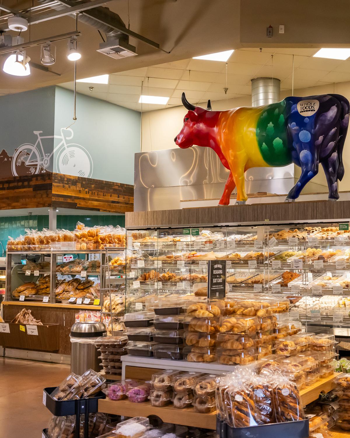 Inside the Hillcrest Whole Foods bakery section, featuring shelves of fresh pastries and a rainbow-colored cow sculpture overhead.