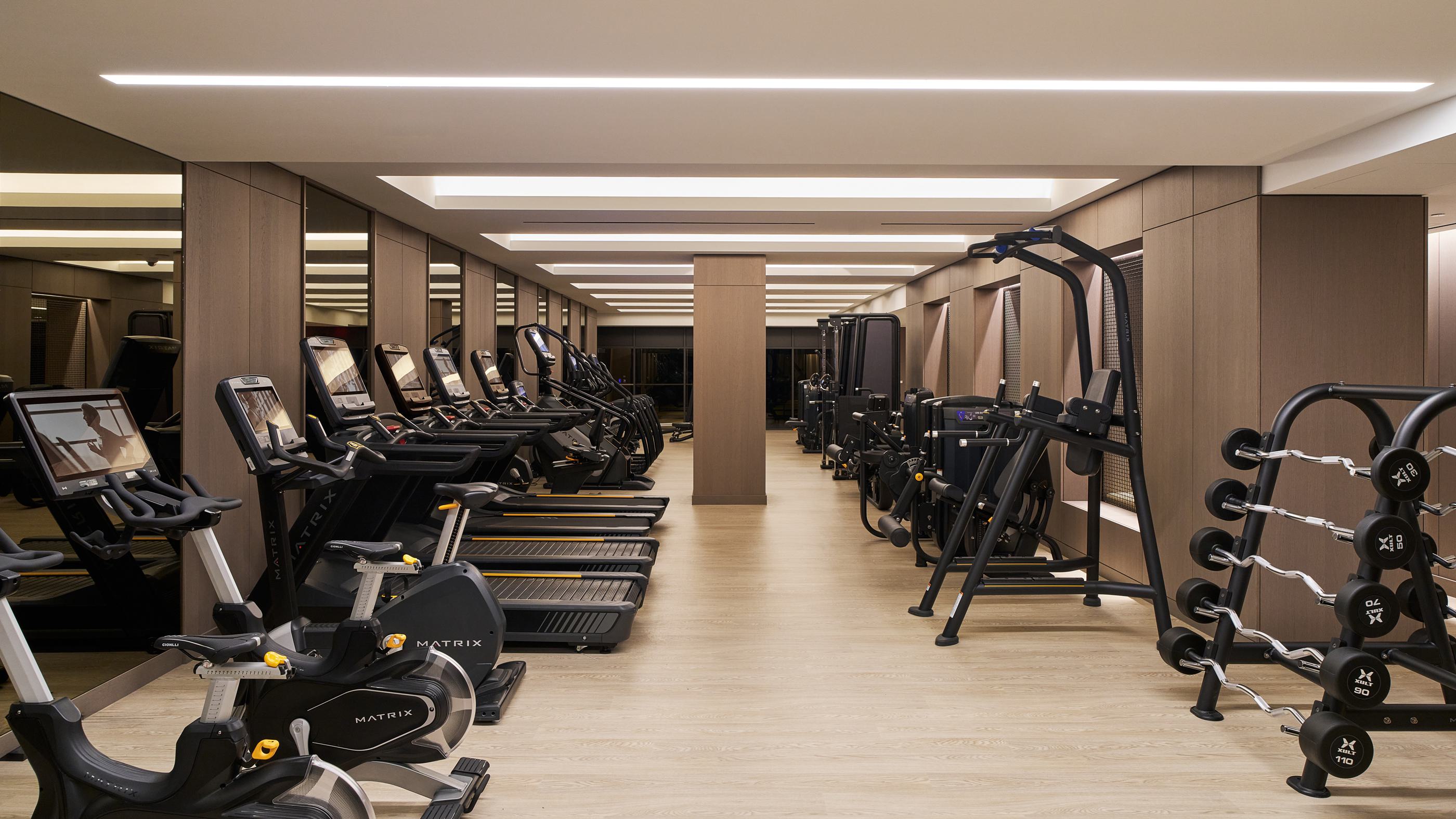 modern gym featuring state-of-the-art cardio and strength training equipment, warm wood paneling, mirrored walls, and soft ambient lighting for a sophisticated workout environment.