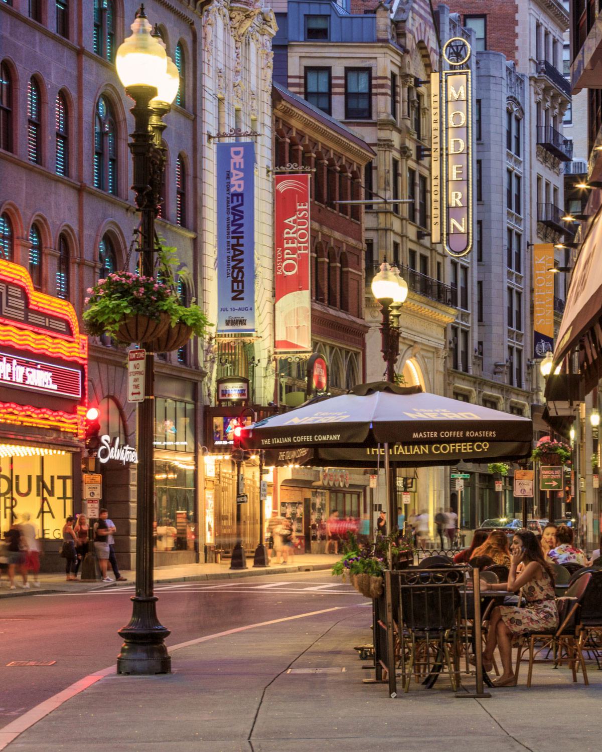 Boston’s Theatre District, featuring the Boston Opera House, illuminated streetlights, café seating, and vibrant signage