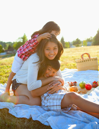 Woman and two young kids picnicking at a grassy park