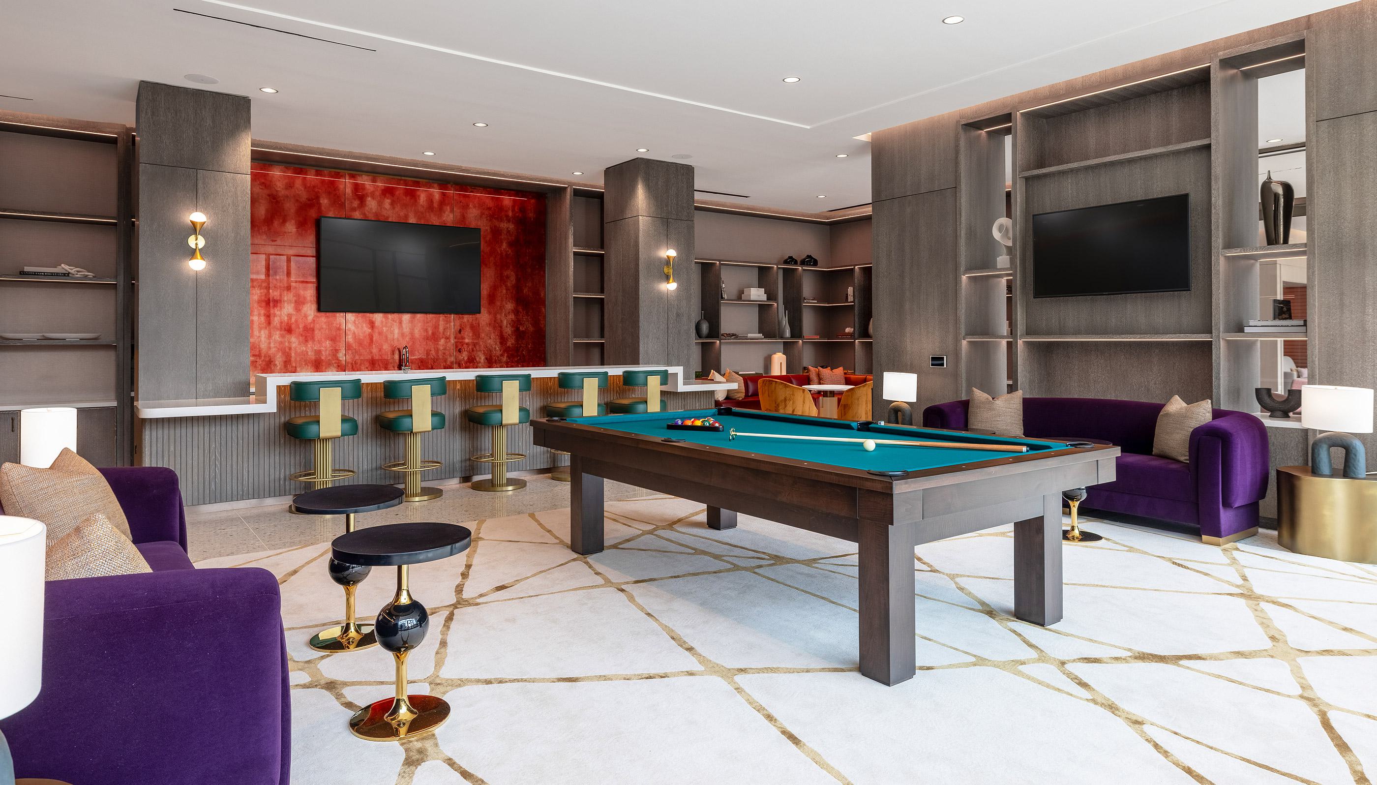 stylish game and media lounge featuring a central pool table, wall-mounted TVs displaying a baseball game, plush seating, and built-in shelving.