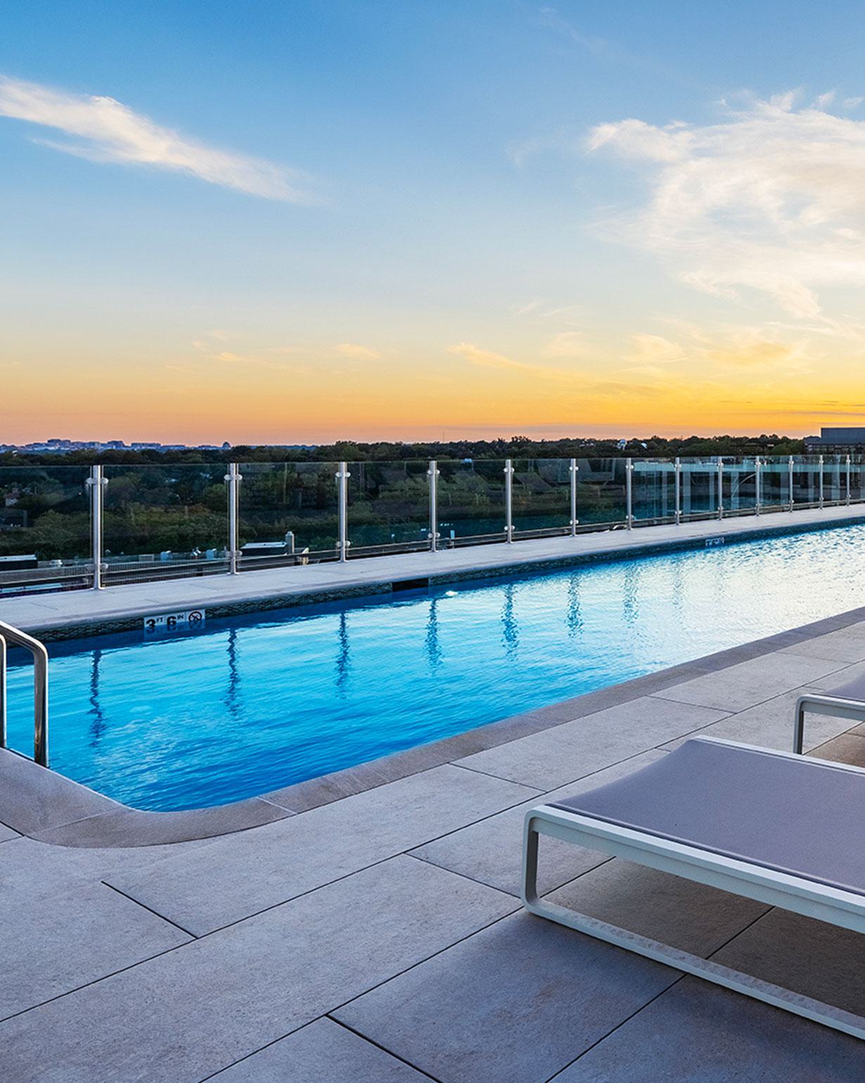 rooftop infinity pool surrounded by white lounge chairs and umbrellas, overlooking a clear blue sky.