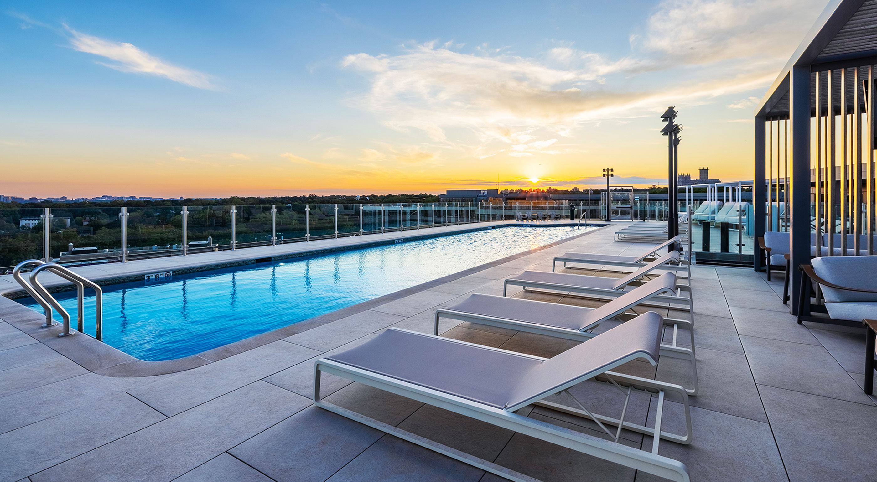 rooftop infinity pool surrounded by white lounge chairs and umbrellas, overlooking a clear blue sky.