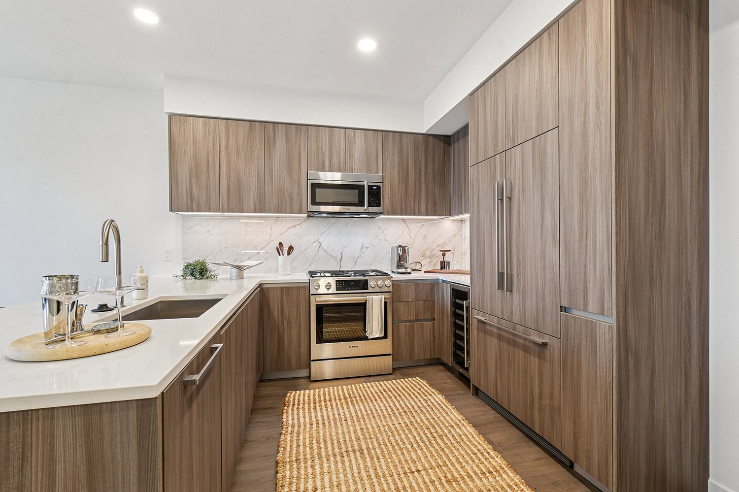 A sleek, modern kitchen with dark wood cabinetry, a large white island with bar seating, and integrated appliances set against a marble backsplash.