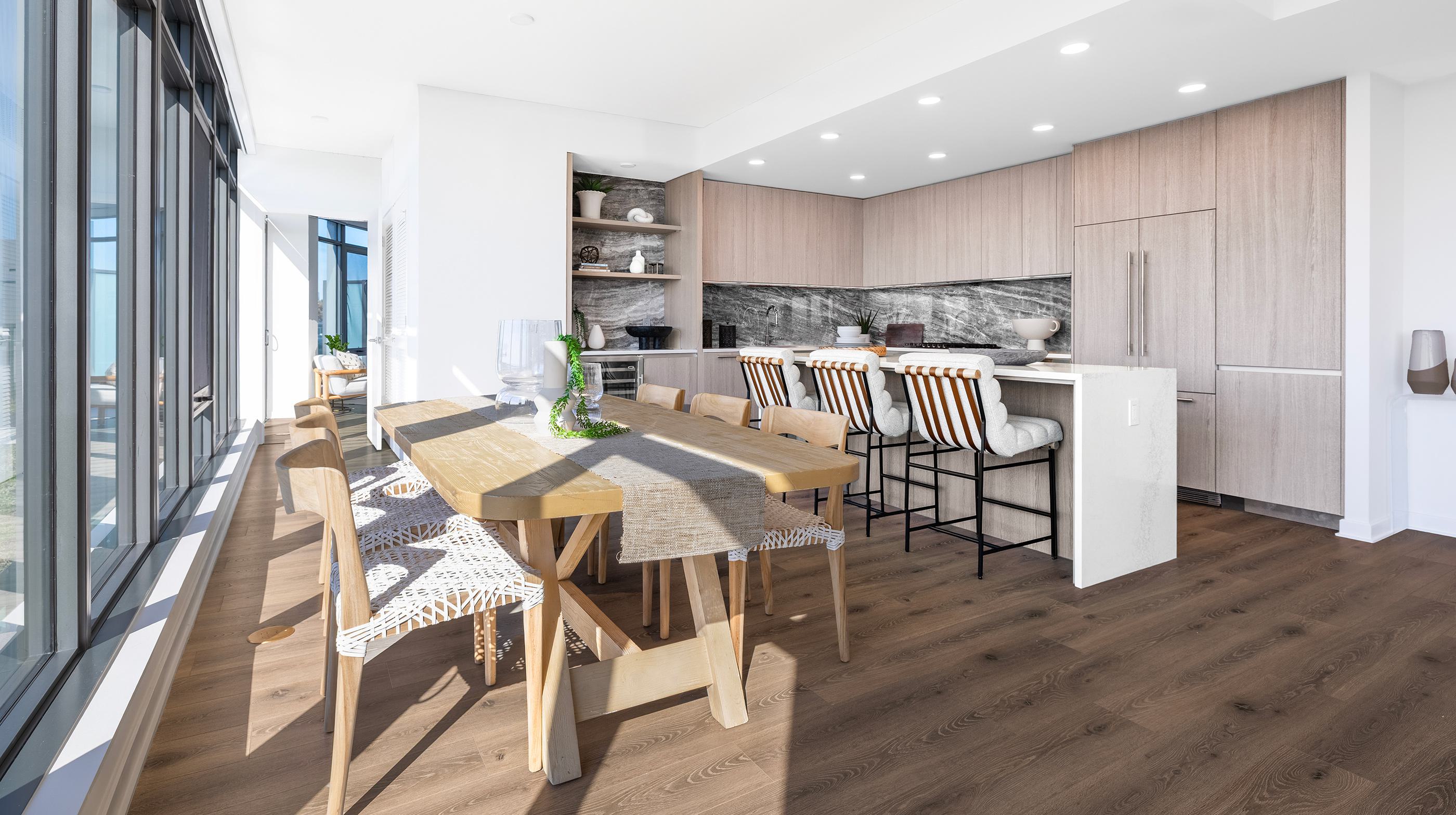 bright, open-concept penthouse living room with a caramel-toned sectional, modern lounge chairs, and floor-to-ceiling windows near a sleek kitchen.