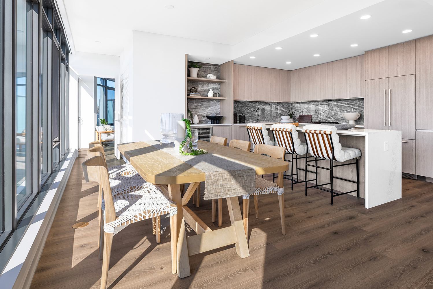 contemporary penthouse kitchen and dining area featuring light wood cabinetry, a marble waterfall island with leather barstools, and a cozy breakfast nook with upholstered chairs.