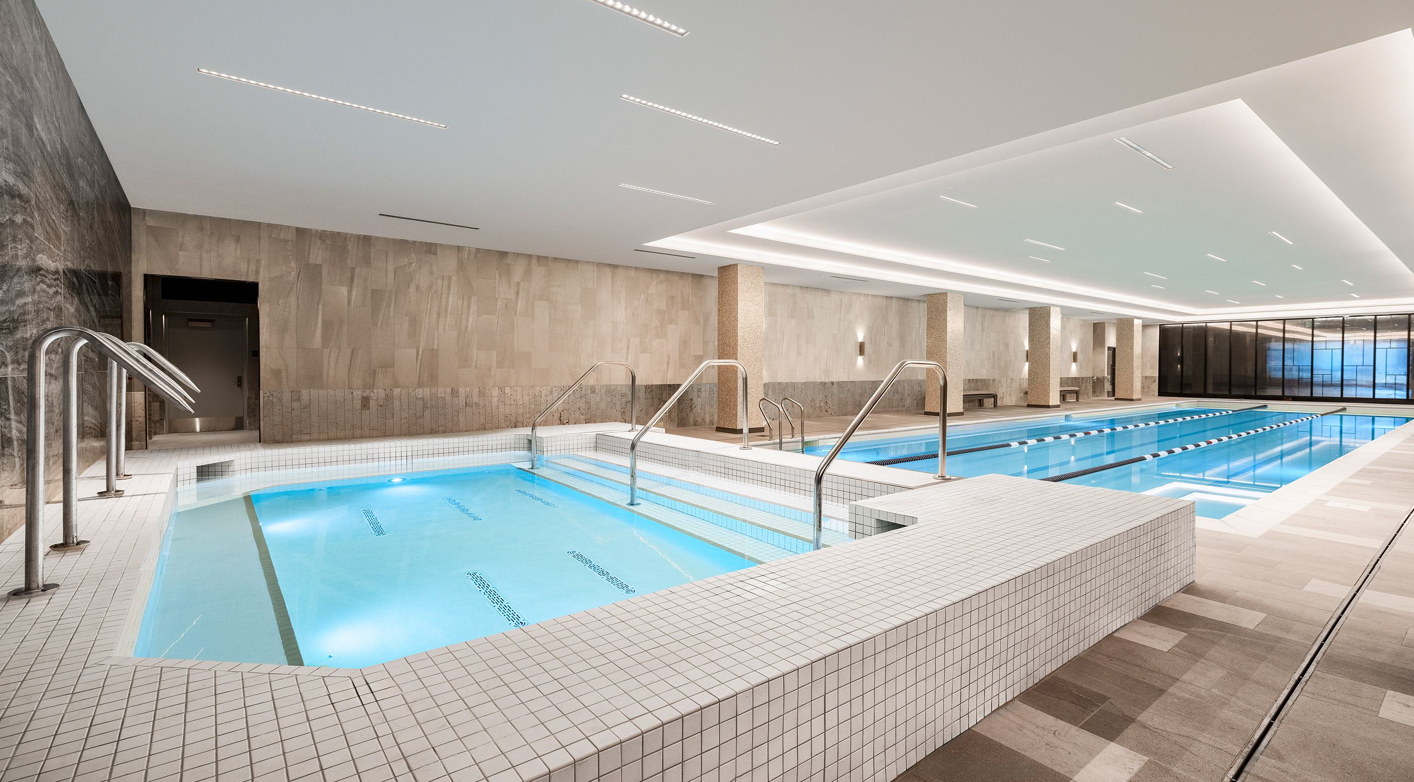 Indoor lap pool at Zephyr in Woodley Park, DC, featuring a serene, spa-inspired design with soft ambient lighting, textured walls, and poolside lounge seating along the perimeter.