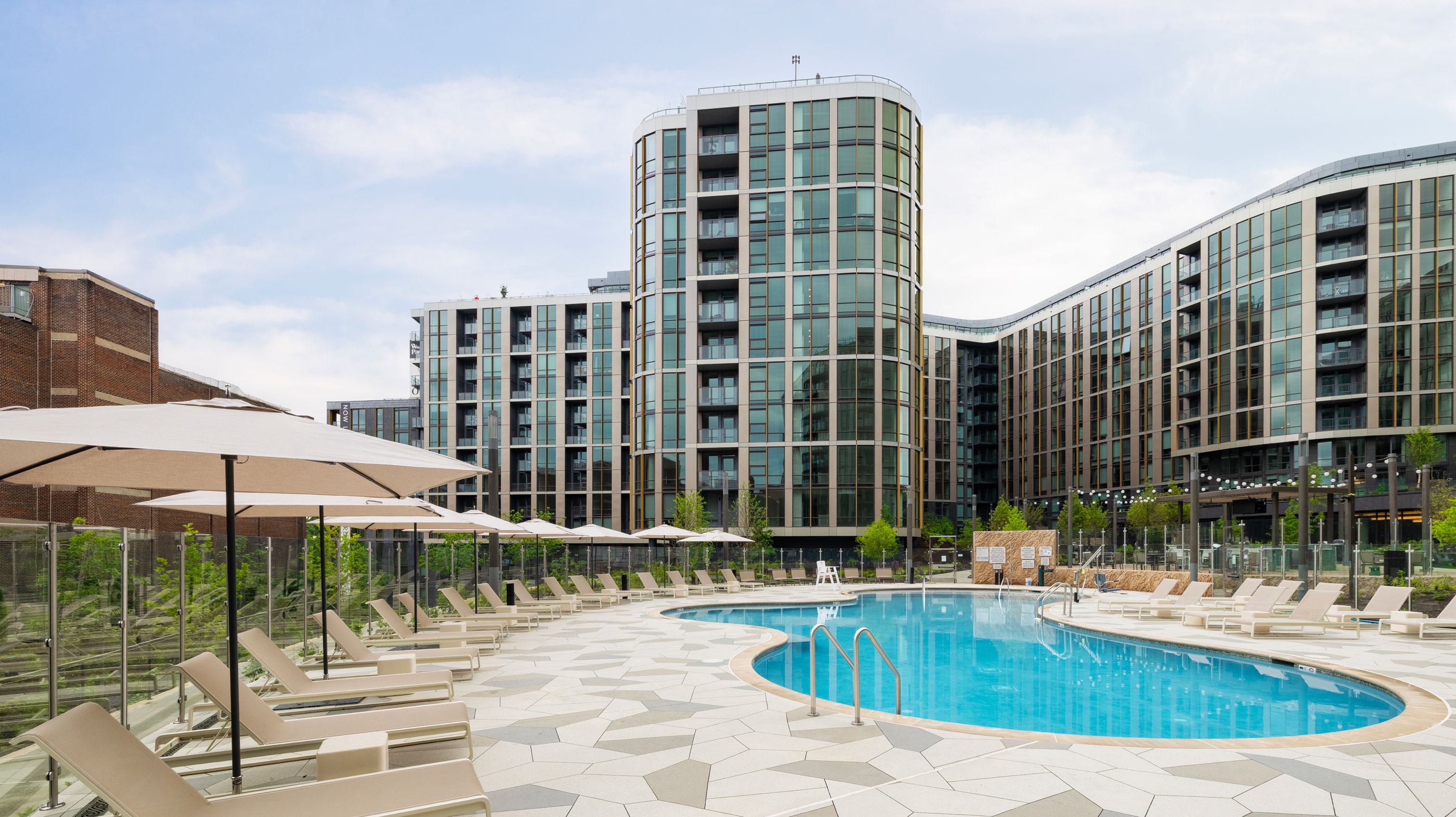 Aerial view of the redeveloped Wardman Park site in Woodley Park, DC, featuring the new Zephyr and Aerie high-rise buildings with sleek glass façades, landscaped courtyards, a resort-style pool, and lush green spaces throughout the property.