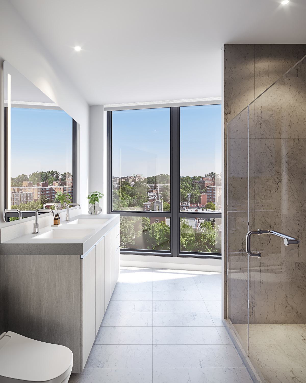 Modern bathroom at Zephyr in Woodley Park, DC, featuring a double vanity with sleek fixtures, a glass-enclosed shower with marble tile, and expansive floor-to-ceiling windows framing views of the city and treetops below.