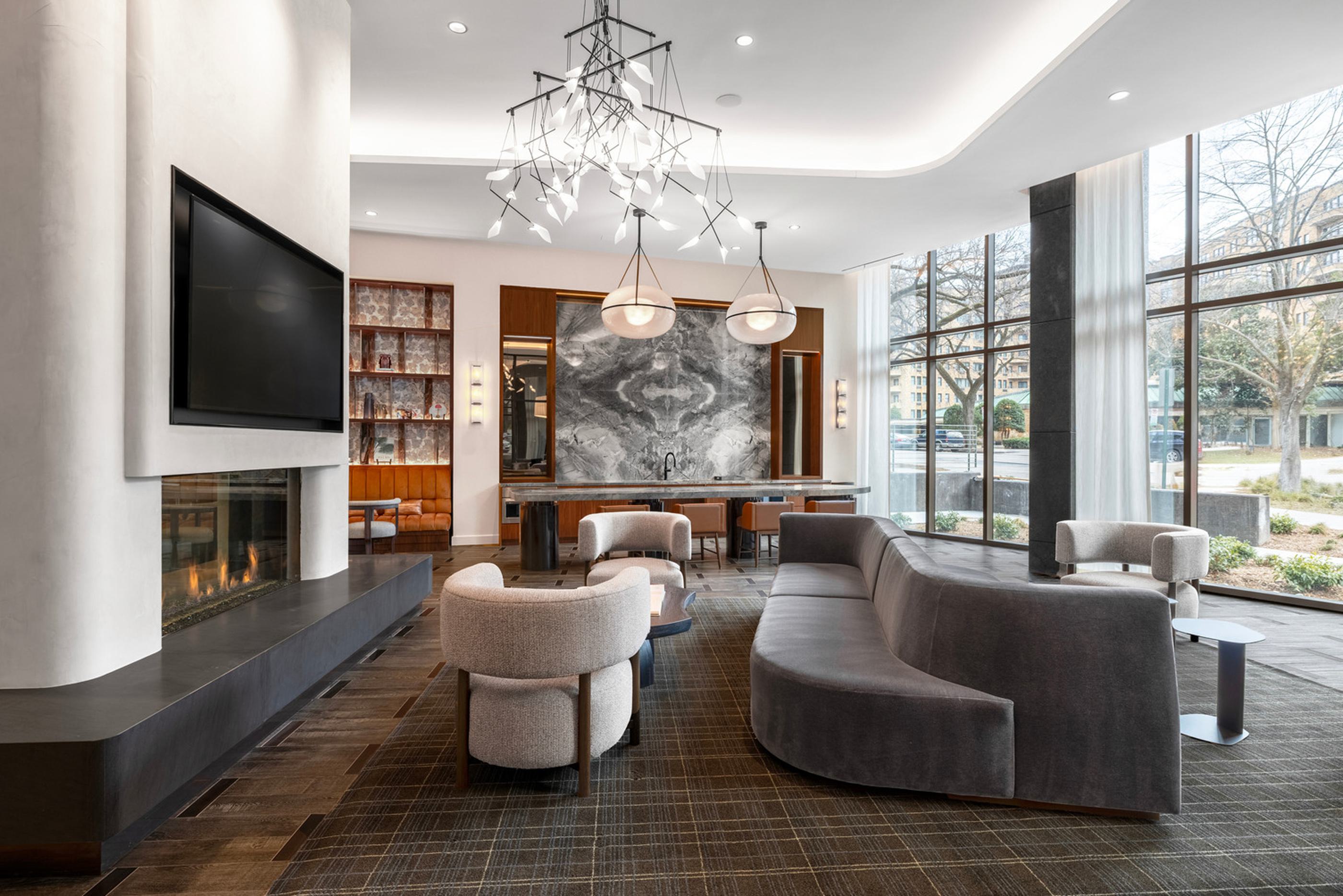 The Observatory lounge at Zephyr in Woodley Park, DC, featuring a circular glass fireplace, plush seating, and floor-to-ceiling windows opening to panoramic views of the city skyline, including the Washington Monument at sunset.