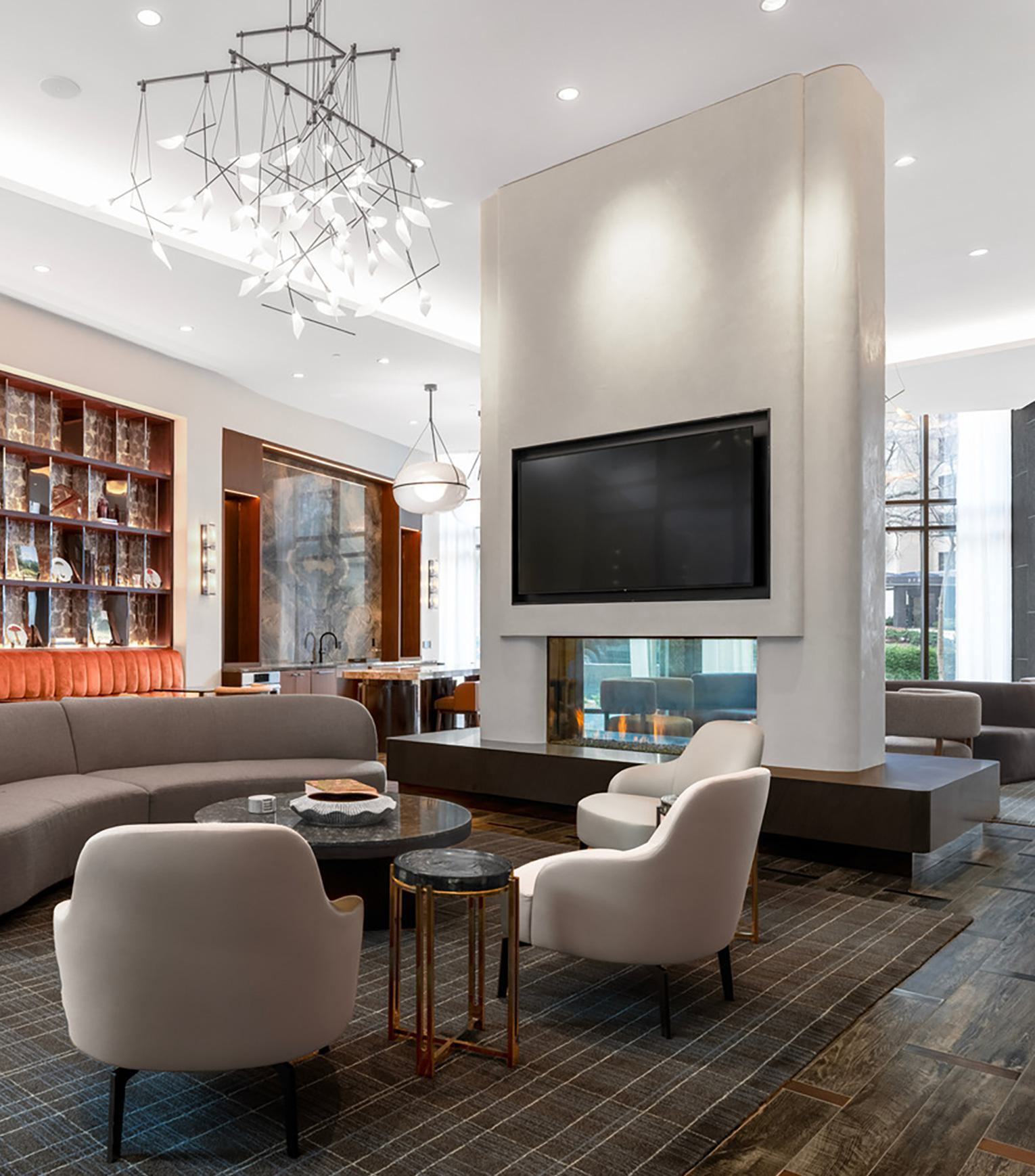 Sophisticated lounge at Zephyr in Woodley Park, DC, featuring a modern double-sided fireplace, plush seating areas, a curated wall display, and floor-to-ceiling windows that bring in natural light and views of the landscaped surroundings.