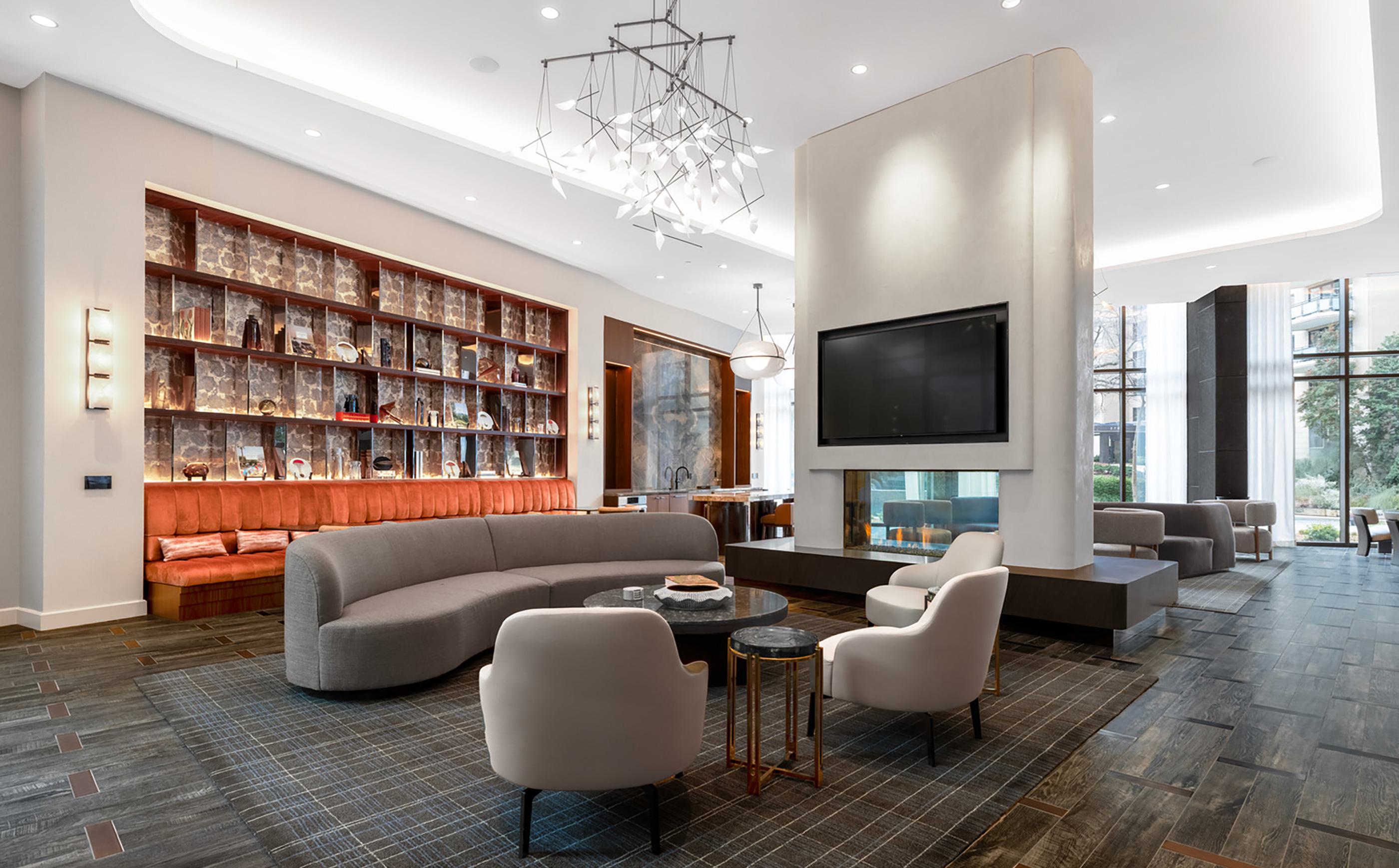 Sophisticated lounge at Zephyr in Woodley Park, DC, featuring a modern double-sided fireplace, plush seating areas, a curated wall display, and floor-to-ceiling windows that bring in natural light and views of the landscaped surroundings.