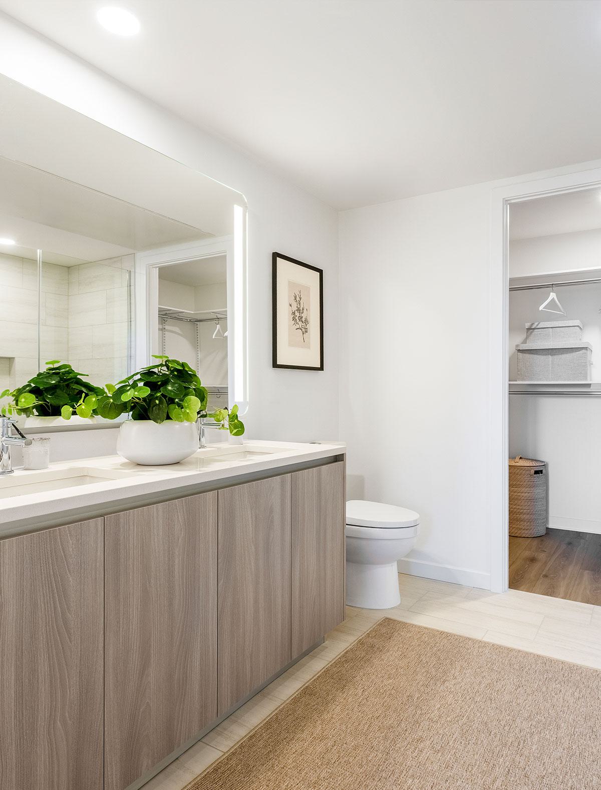 Modern bathroom at Zephyr in Woodley Park, DC, featuring a double vanity with sleek fixtures, a glass-enclosed shower with marble tile, and expansive floor-to-ceiling windows framing views of the city and treetops below.
