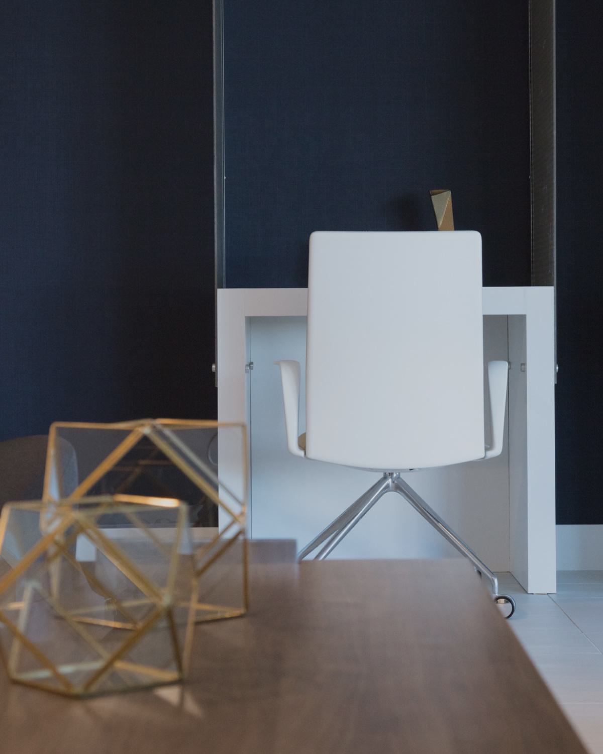 Cozy lounge and work area at The Triton Apartments featuring a modern white desk with chair, navy accent wall, geometric decor, and comfortable seating with a yellow pillow.