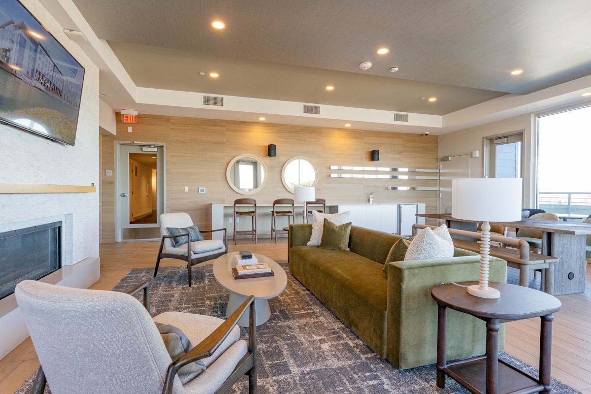 Elegant lounge at The Triton Apartments featuring modern decor, a wood accent wall with The Triton logo, statement lighting, stylish seating in blue and patterned chairs, and a welcoming reception desk.