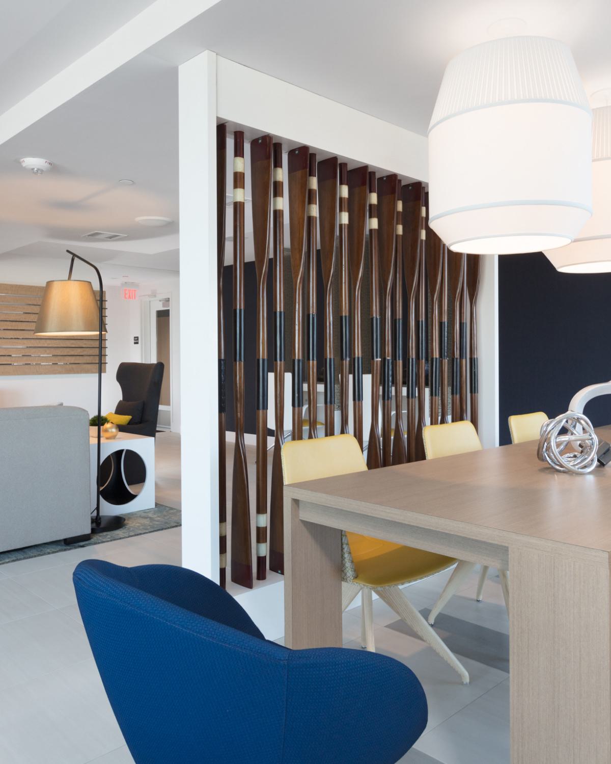 Contemporary clubhouse detail at The Triton Apartments with a wood dining table, colorful chairs, sculptural decor, and a unique divider made of decorative oars.