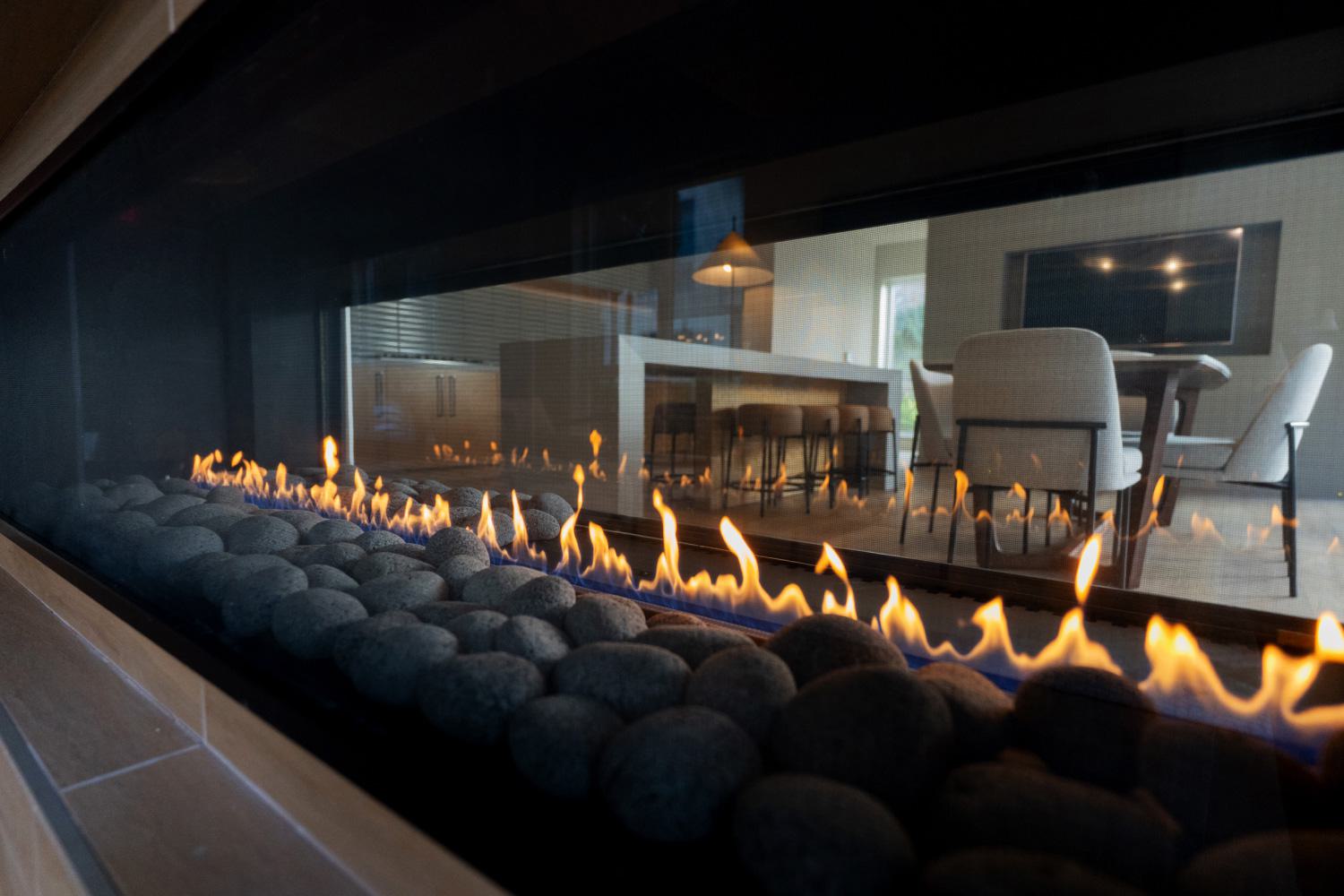 Stylish dining area with a wooden table set for two, modern gray chairs, a tufted sofa in the background, and a sculptural light fixture with decorative wall accents.