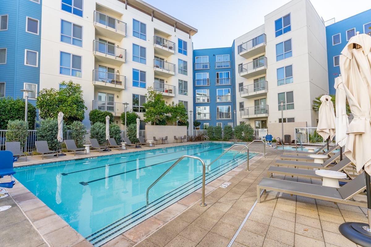 Contemporary kitchen at The Triton Apartments with sleek wood cabinetry, stainless steel appliances, a tiled backsplash, and a large island countertop accented by modern decor.