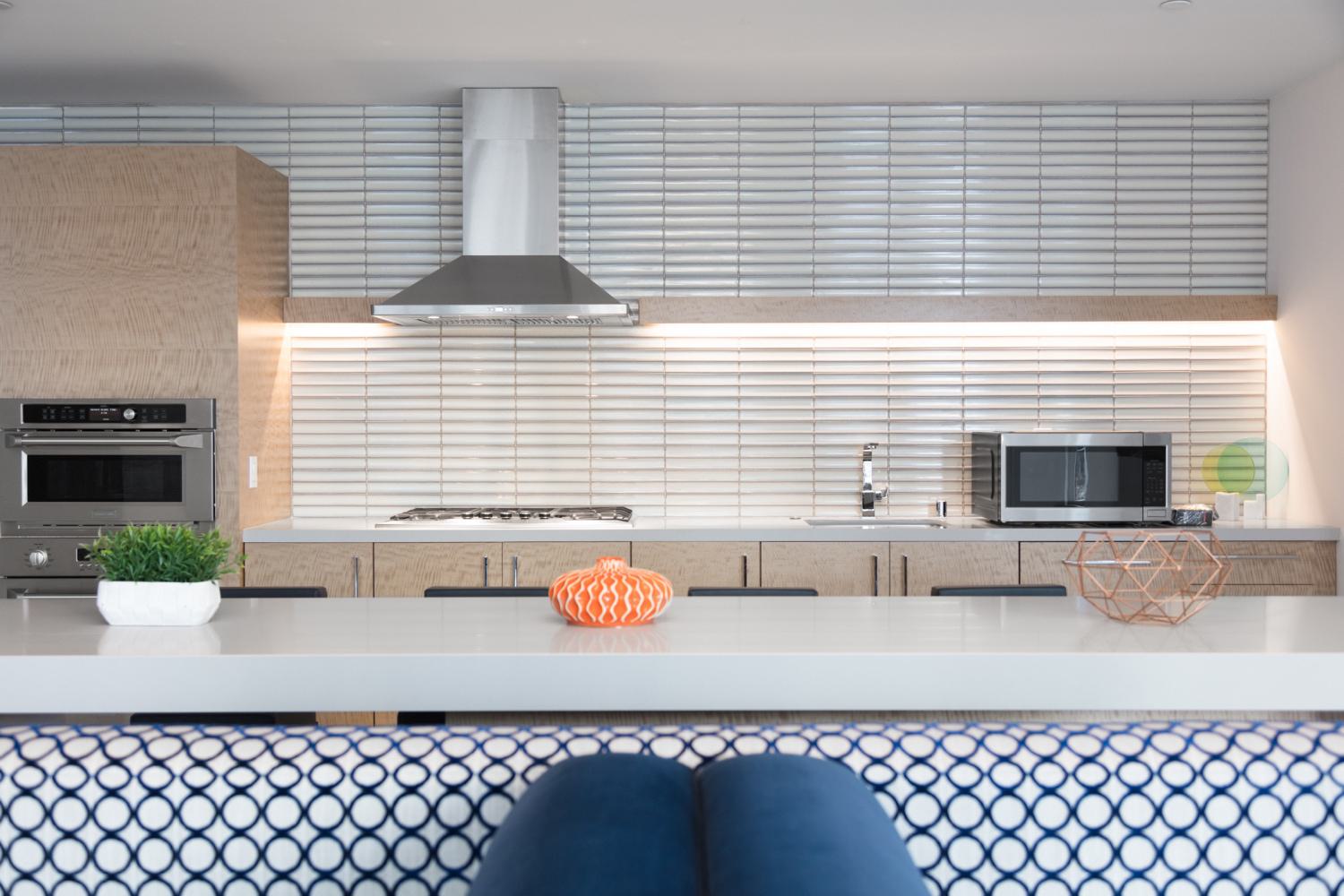 Contemporary kitchen at The Triton Apartments with sleek wood cabinetry, stainless steel appliances, a tiled backsplash, and a large island countertop accented by modern decor.