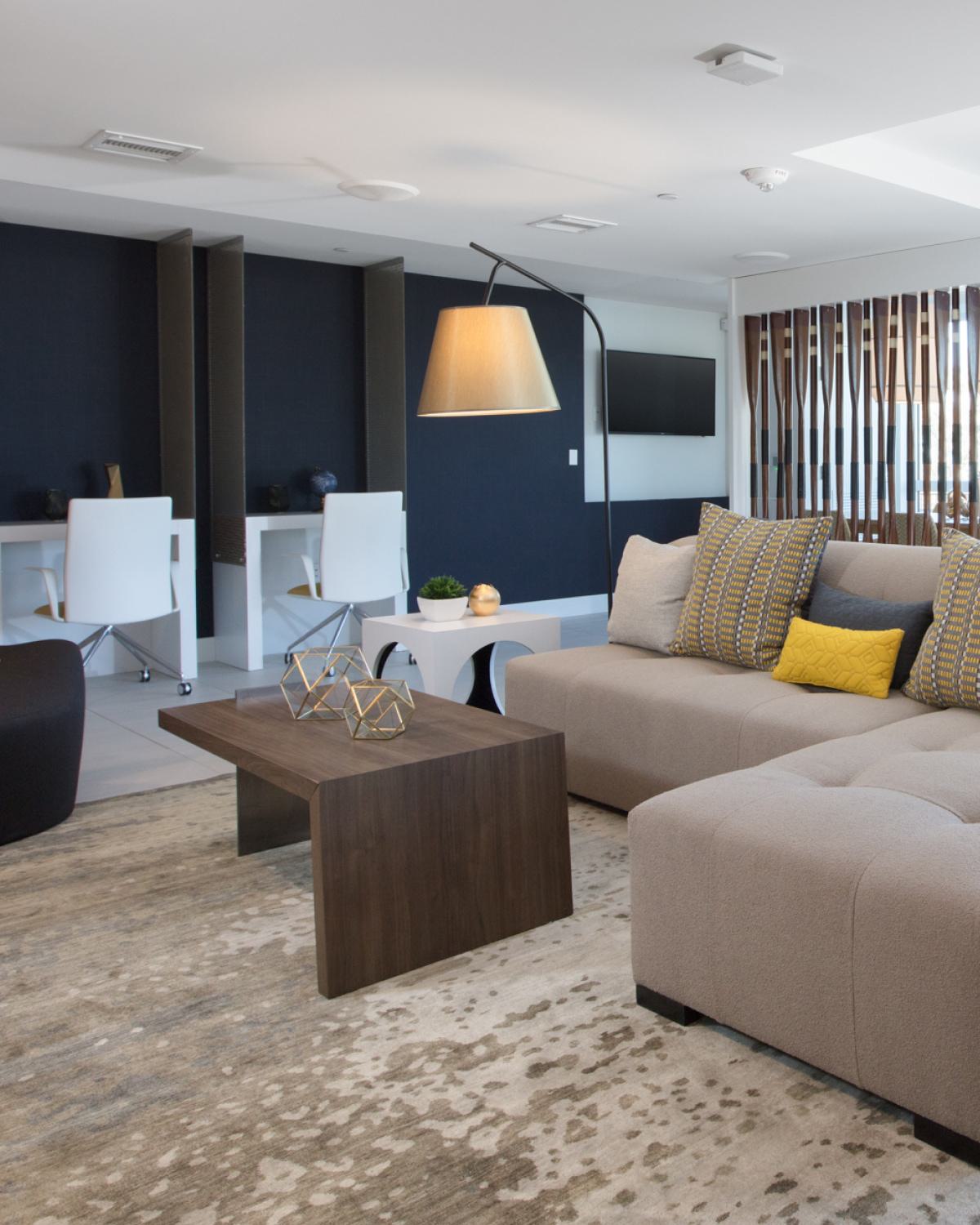 Modern community clubhouse at The Triton Apartments featuring a spacious lounge with contemporary seating, workstations, large windows for natural light, and stylish decor.