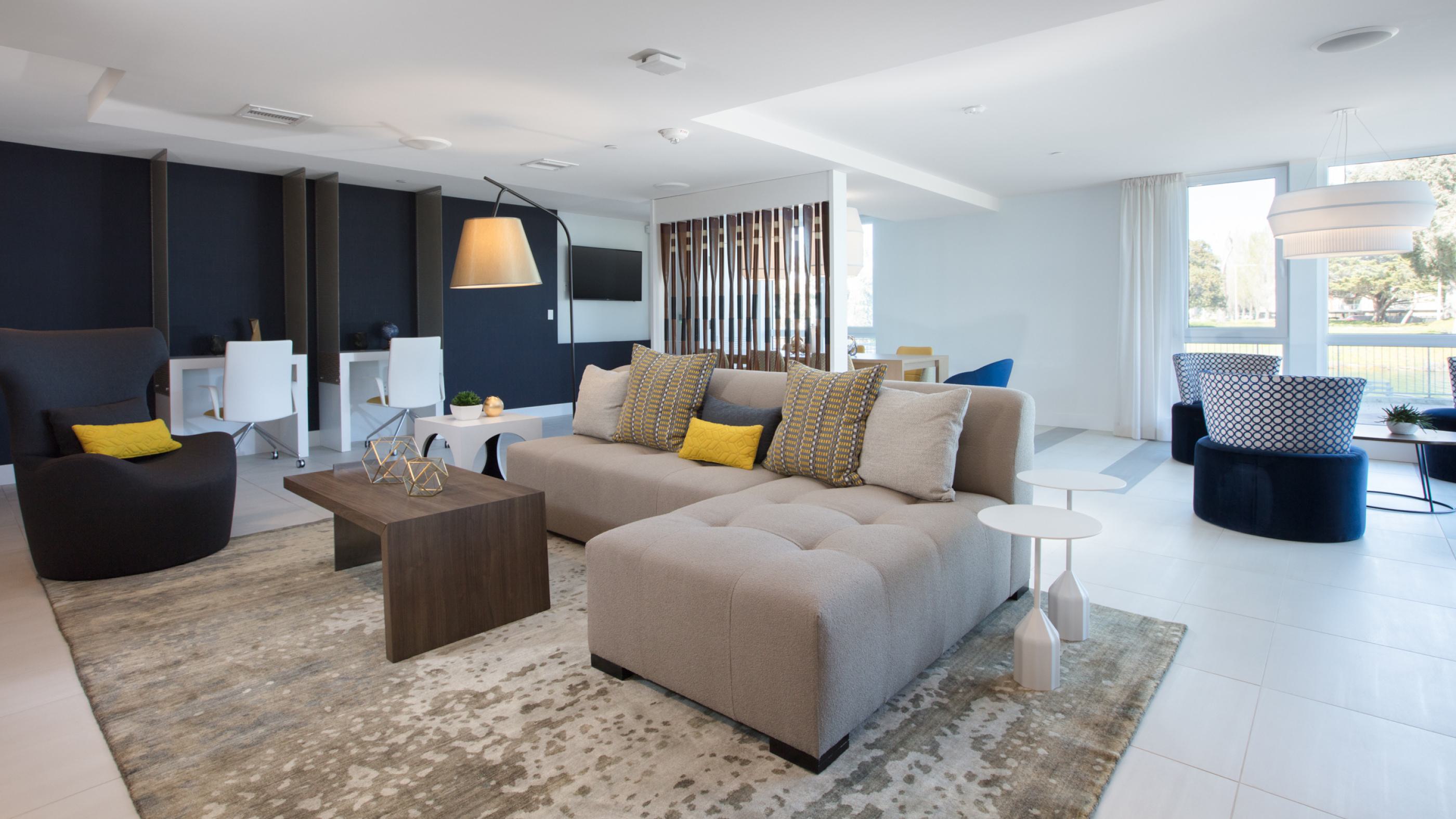 Modern community clubhouse at The Triton Apartments featuring a spacious lounge with contemporary seating, workstations, large windows for natural light, and stylish decor.