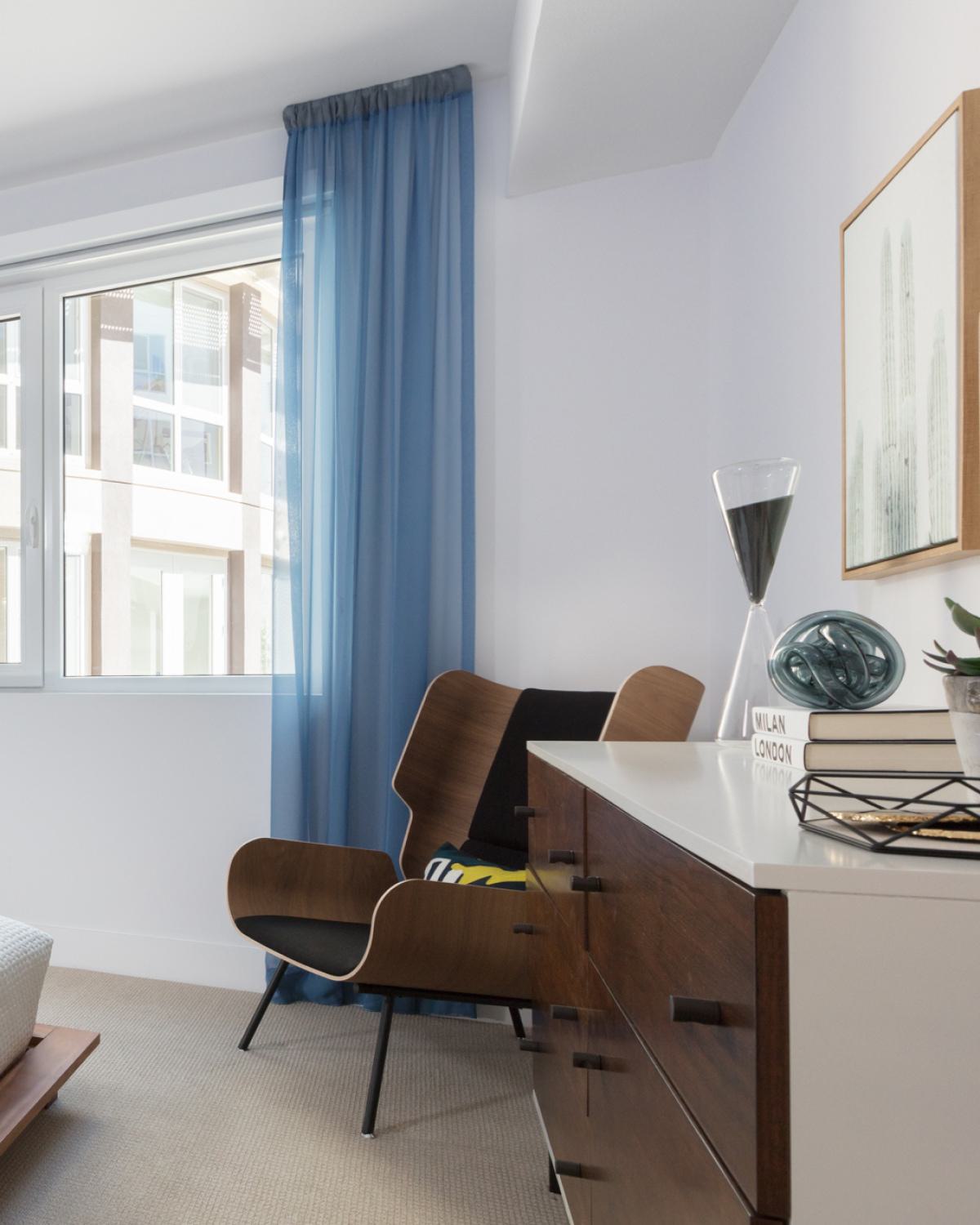 Bright modern apartment living room at The Triton featuring a neutral sofa with colorful pillows, open kitchen with stainless steel appliances, dining area with glass table, and contemporary decor accents.