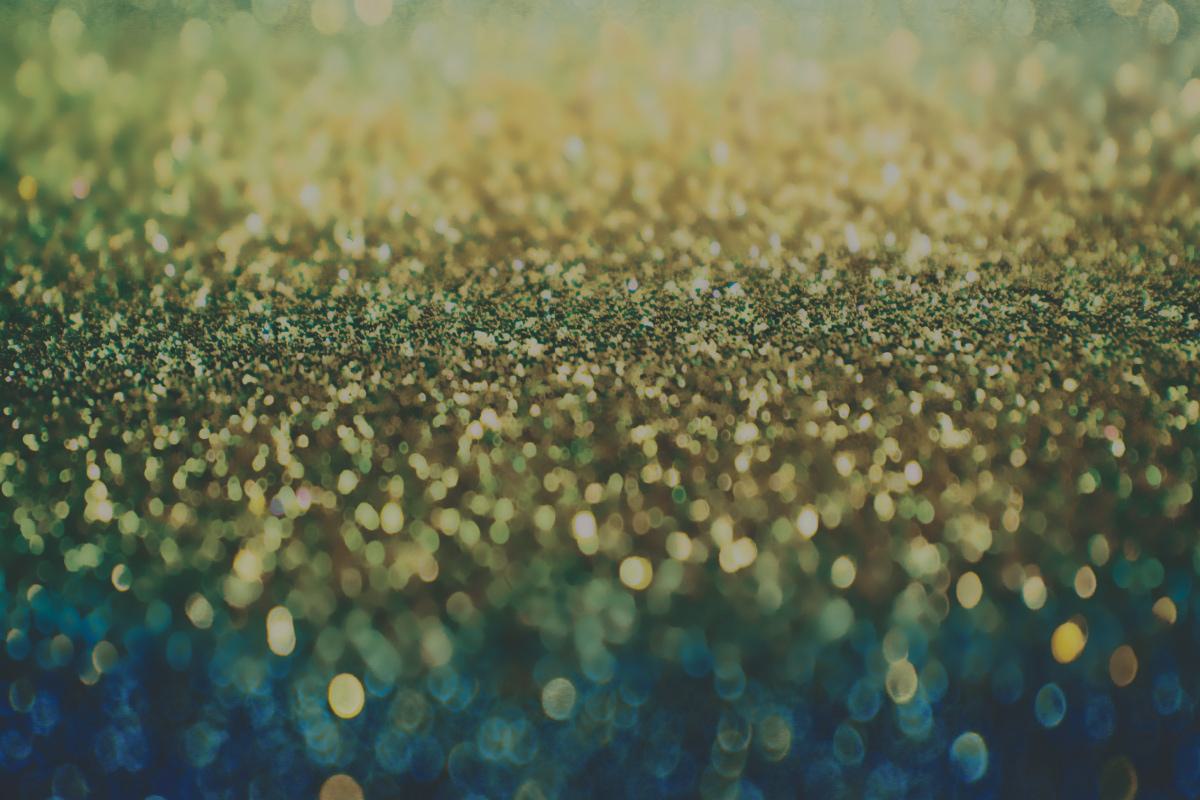 Abstract background of blurred gold and green glitter creating a shimmering, bokeh effect.