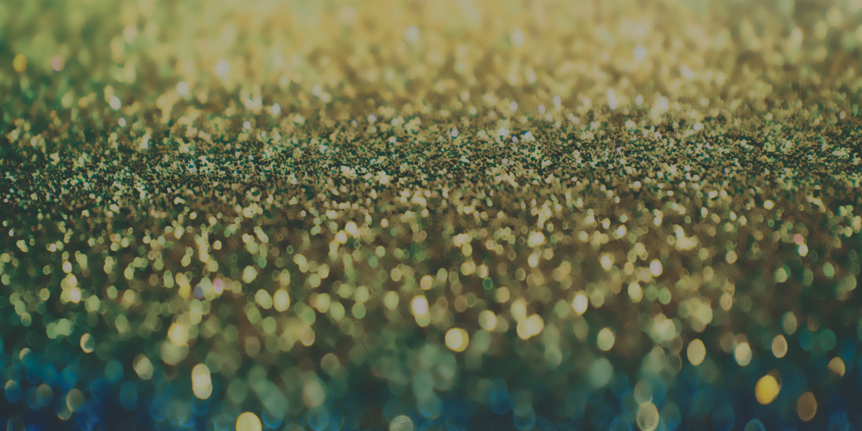 Abstract background of blurred gold and green glitter creating a shimmering, bokeh effect.