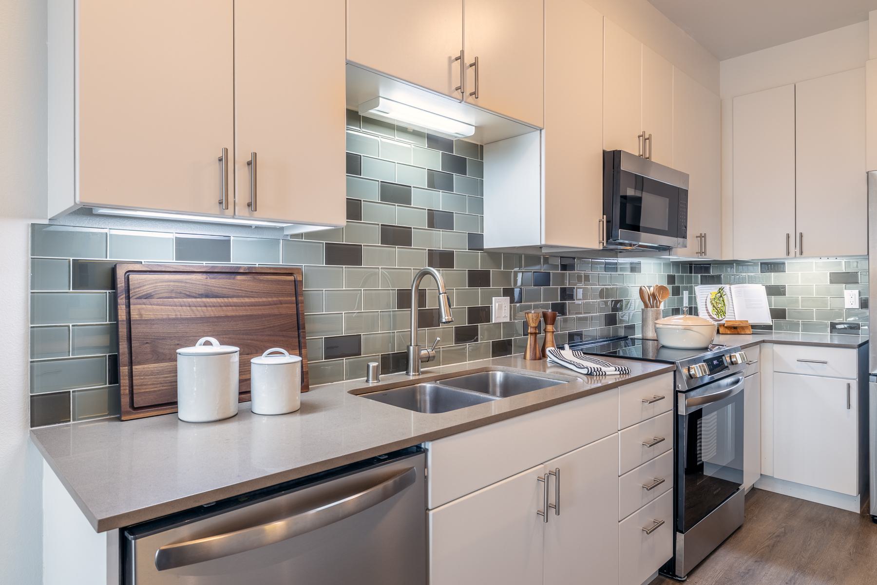 Cozy bedroom with neutral plaid bedding, a potted plant, and a large window offering natural light and views of a green hillside in Ballard in the distance.