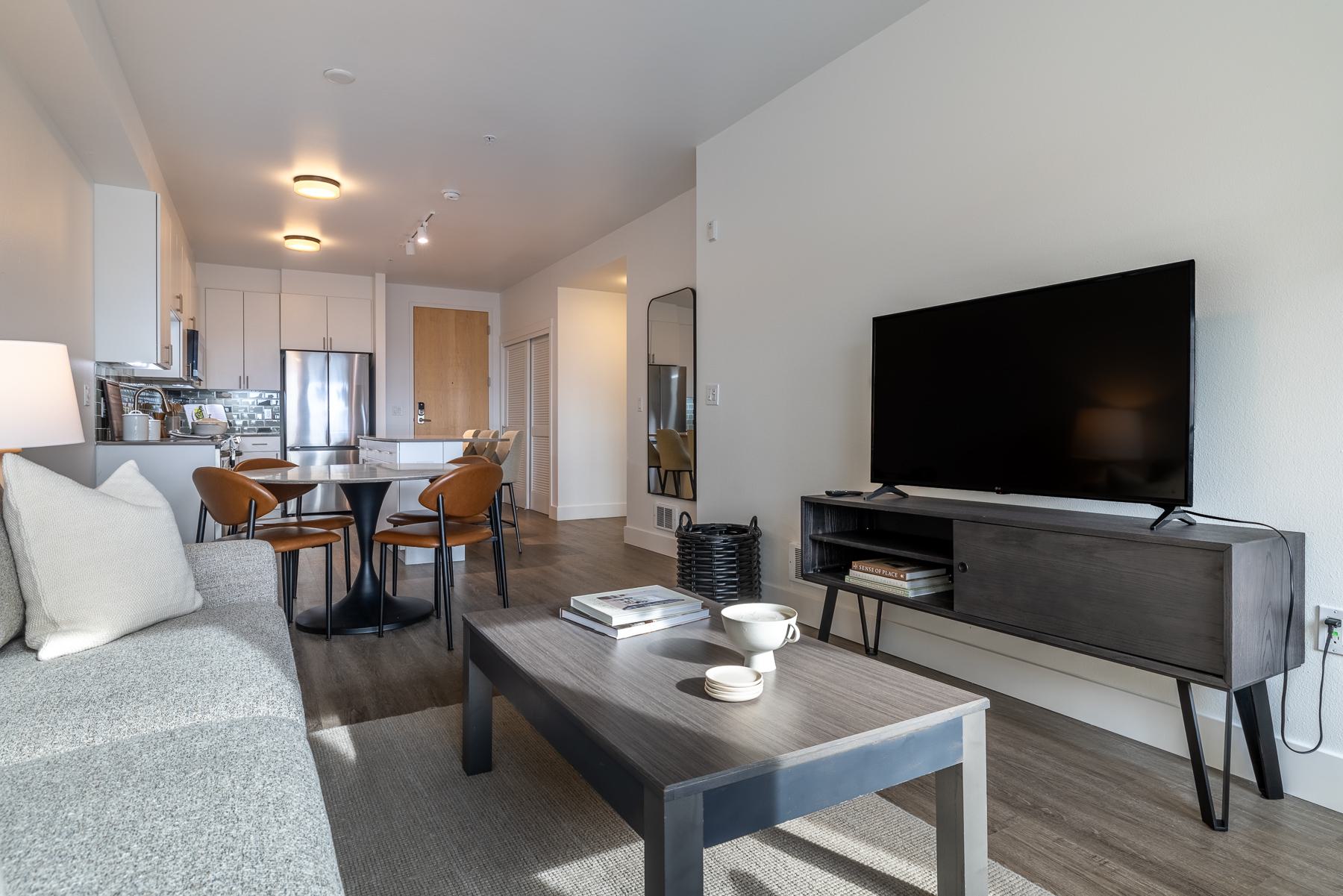 Cozy modern living room with a sectional sofa, wood accents, a mounted TV, and access to a private balcony with views of surrounding neighborhood in Ballard, Seattle.
