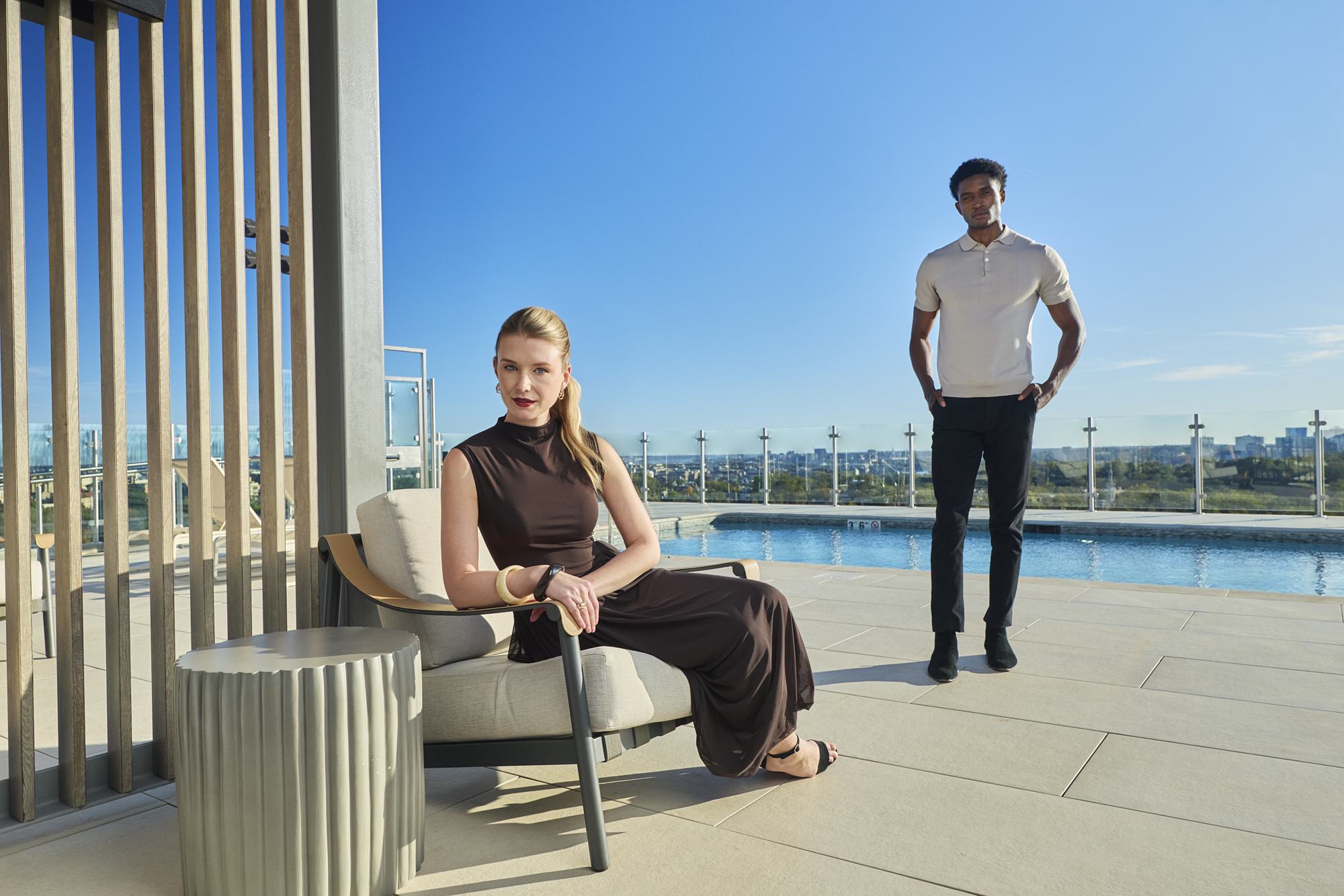 rooftop infinity pool surrounded by white lounge chairs and umbrellas, overlooking a clear blue sky.