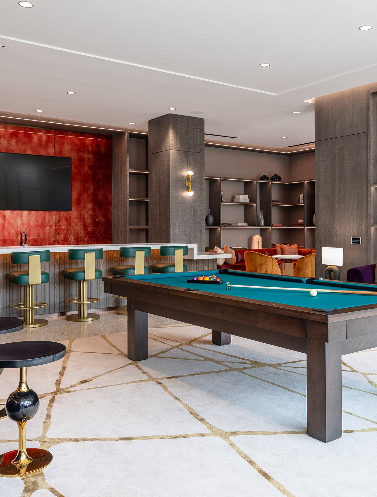 stylish game and media lounge featuring a central pool table, wall-mounted TVs displaying a baseball game, plush seating, and built-in shelving.