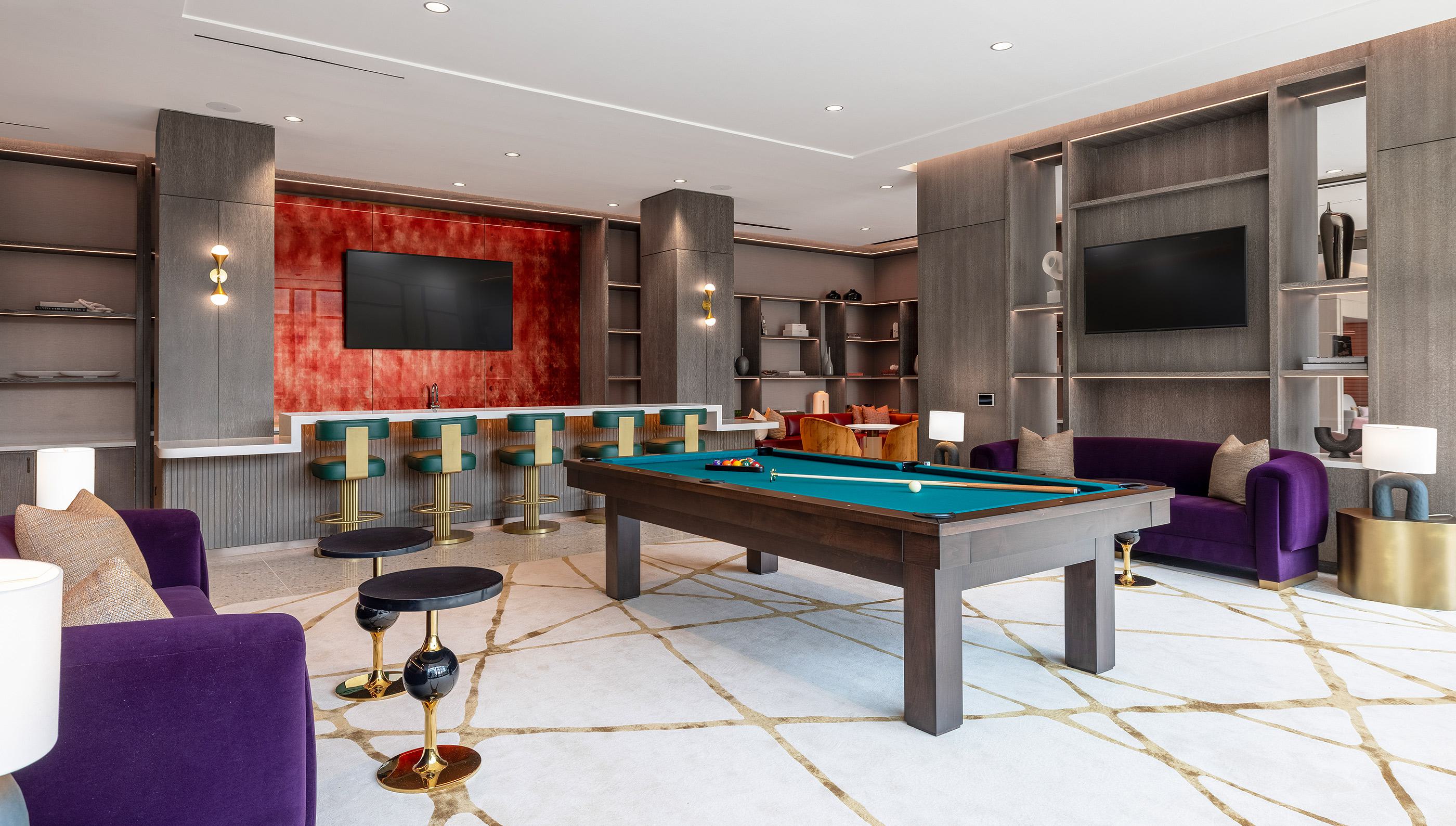 stylish game and media lounge featuring a central pool table, wall-mounted TVs displaying a baseball game, plush seating, and built-in shelving.