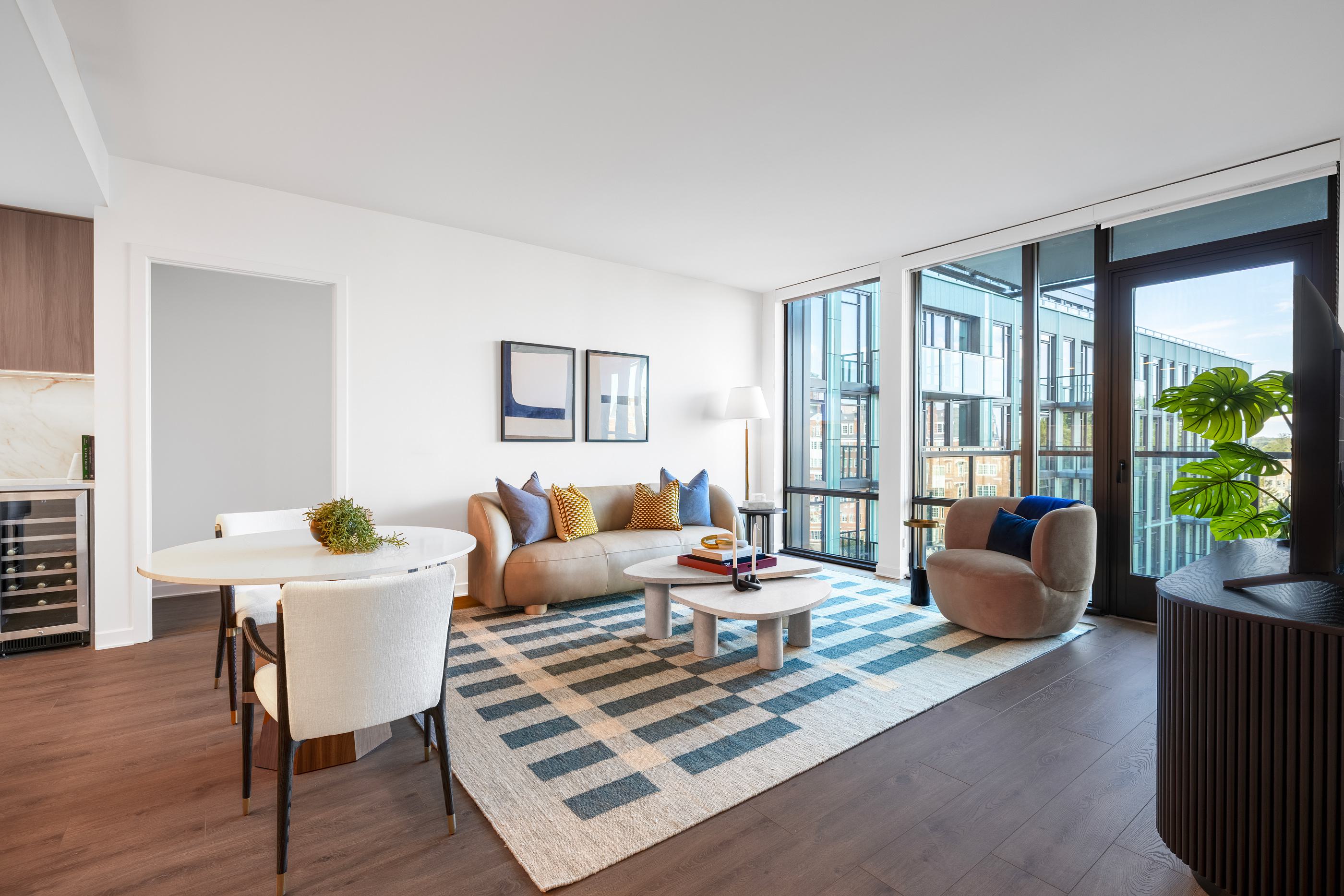 elegant open-concept living space with a modern kitchen, cozy seating area, and a wood dining table set beside floor-to-ceiling windows.