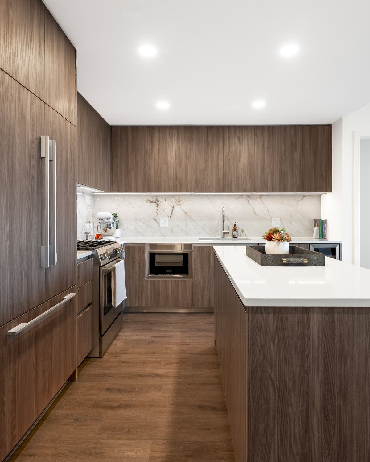  sleek, modern kitchen with dark wood cabinetry, a large white island with bar seating, and integrated appliances set against a marble backsplash