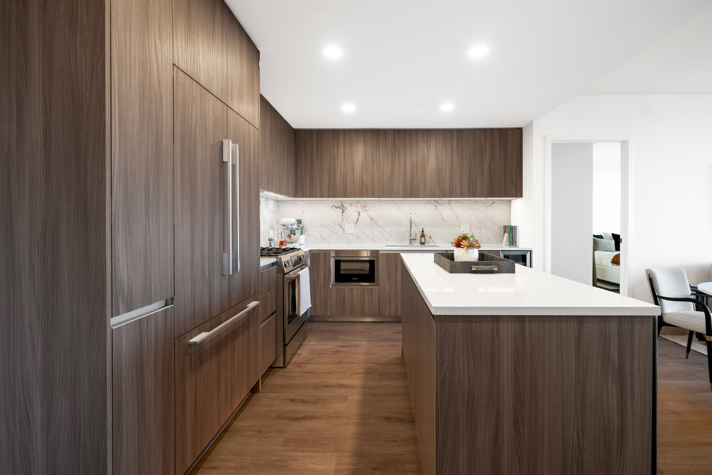 sleek, modern kitchen with dark wood cabinetry, a large white island with bar seating, and integrated appliances set against a marble backsplash