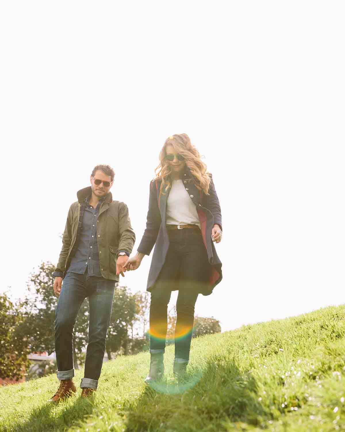 A man and woman holding hands while walking down a grassy hill on a sunny day.