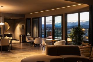 Sunset lounge with cozy seating and floor-to-ceiling windows offering a sweeping view of RiNo, Denver, with city lights and the Rocky Mountains in the distance.