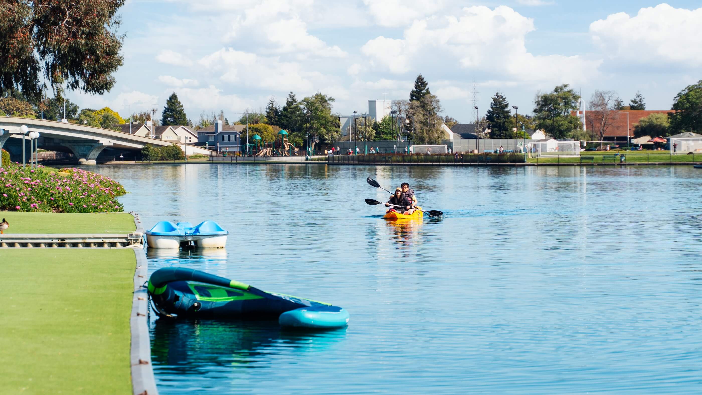 Private dock on the Foster City lagoon beside The Triton Apartments, featuring a boat with a red canopy tied along the waterfront under a clear blue sky.