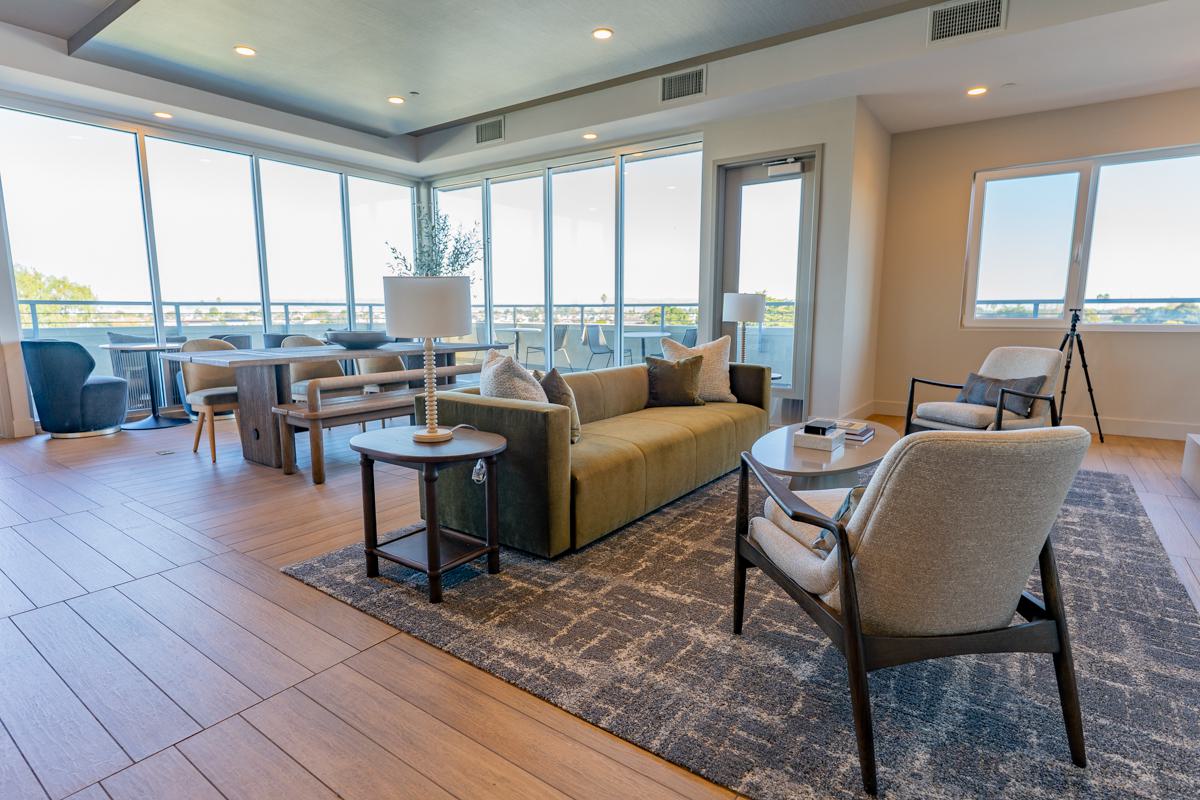 Sleek business lounge at The Triton Apartments featuring a modern kitchen with stainless steel appliances, a cozy fireplace, stylish blue seating, and contemporary lighting.