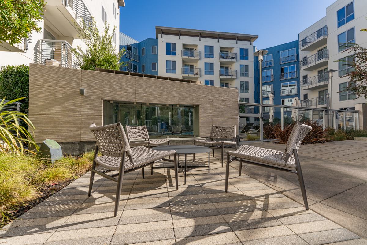 Courtyard at The Triton Apartments featuring a modern outdoor fireplace with glass enclosure, lounge chairs, and surrounding apartment buildings with illuminated windows.