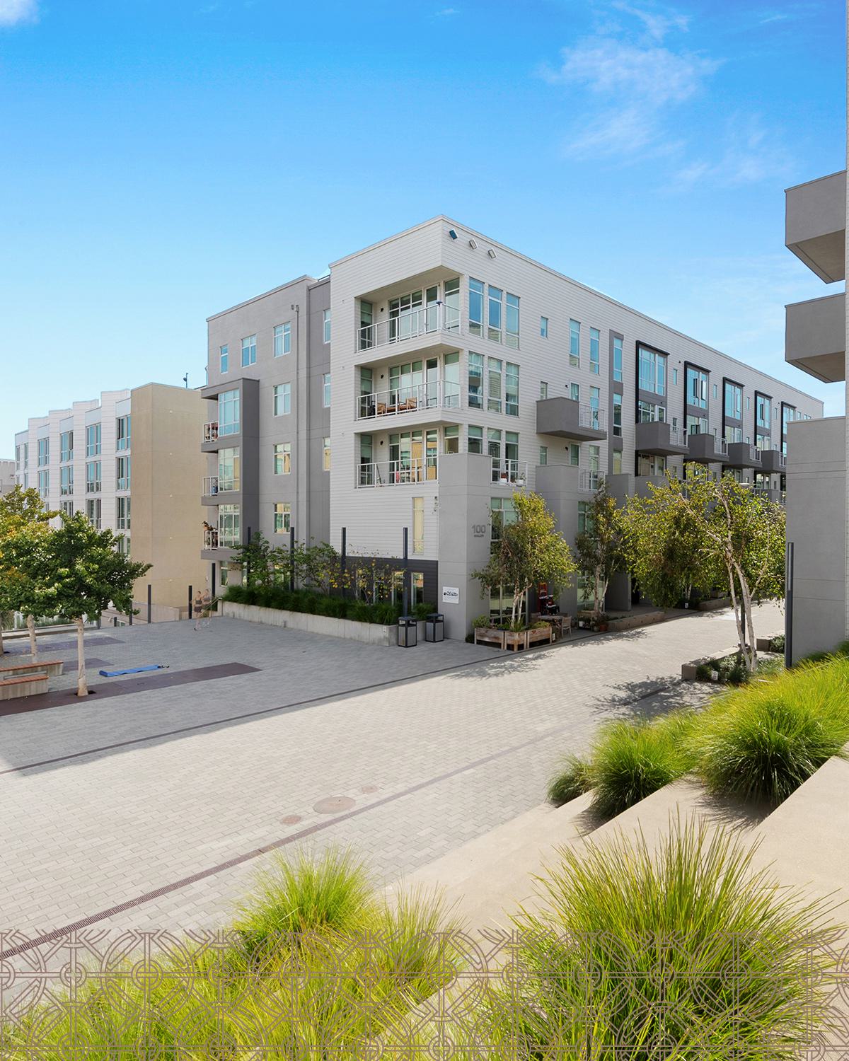 Alchemy contemporary apartment building in Hayes Valley with clean lines, large windows, and private balconies, framed by sleek siding and light neutral tones. Trees line the paved courtyard below, giving the space a modern, walkable neighborhood feel.