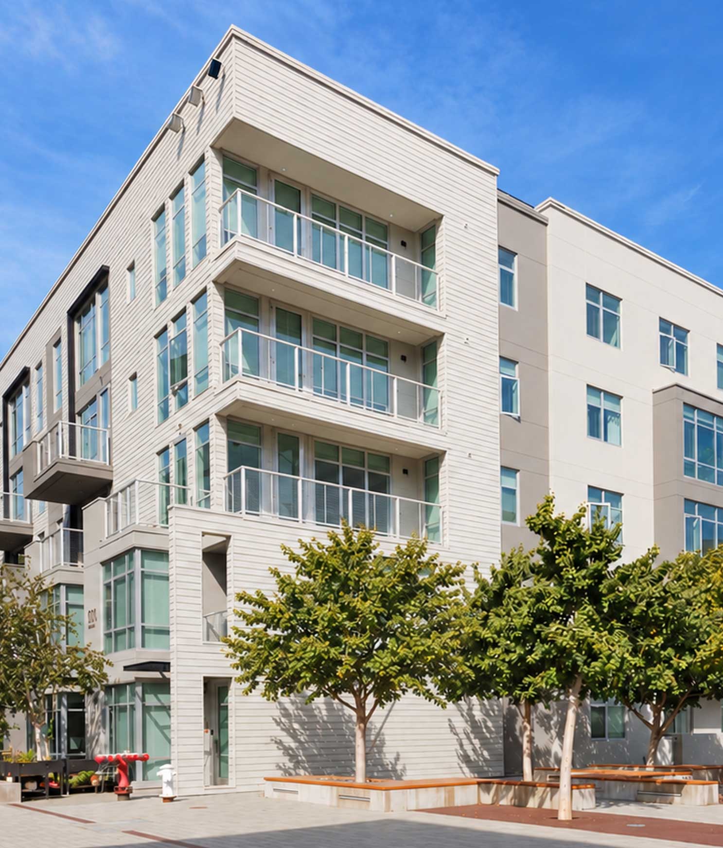 Alchemy contemporary apartment building in Hayes Valley with clean lines, large windows, and private balconies, framed by sleek siding and light neutral tones. Young trees line the paved courtyard below, giving the space a modern, walkable neighborhood feel.