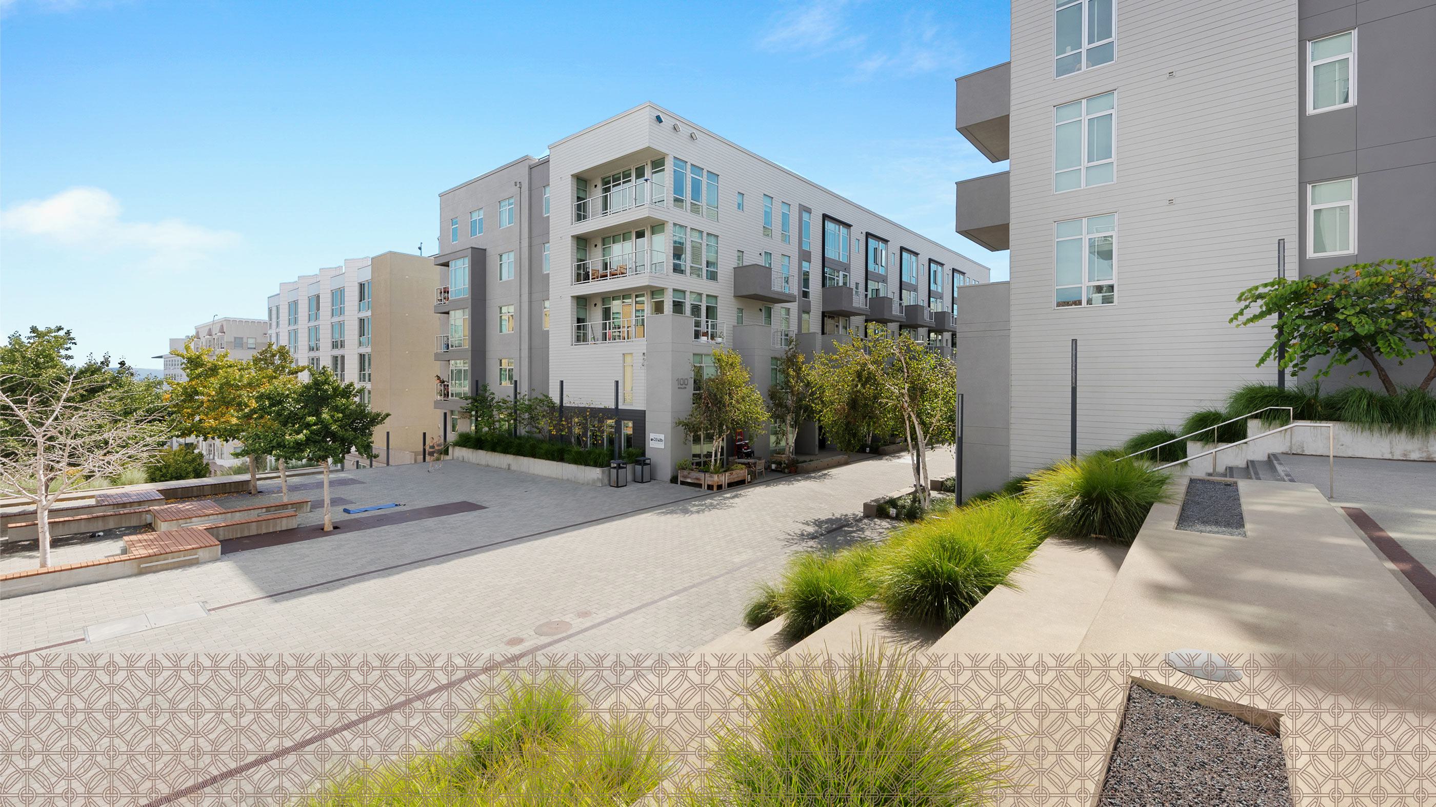 Alchemy contemporary apartment building in Hayes Valley with clean lines, large windows, and private balconies, framed by sleek siding and light neutral tones. Trees line the paved courtyard below, giving the space a modern, walkable neighborhood feel.
